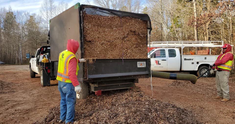 A man in a yellow vest is standing next to a dump truck filled with dirt.