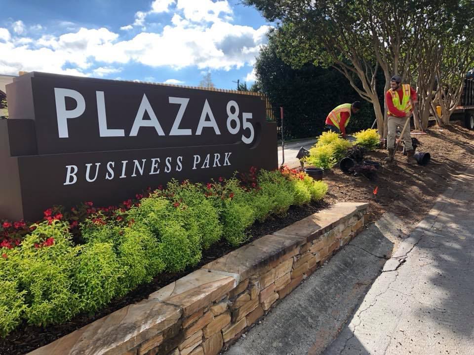A sign for plaza 85 business park is surrounded by flowers