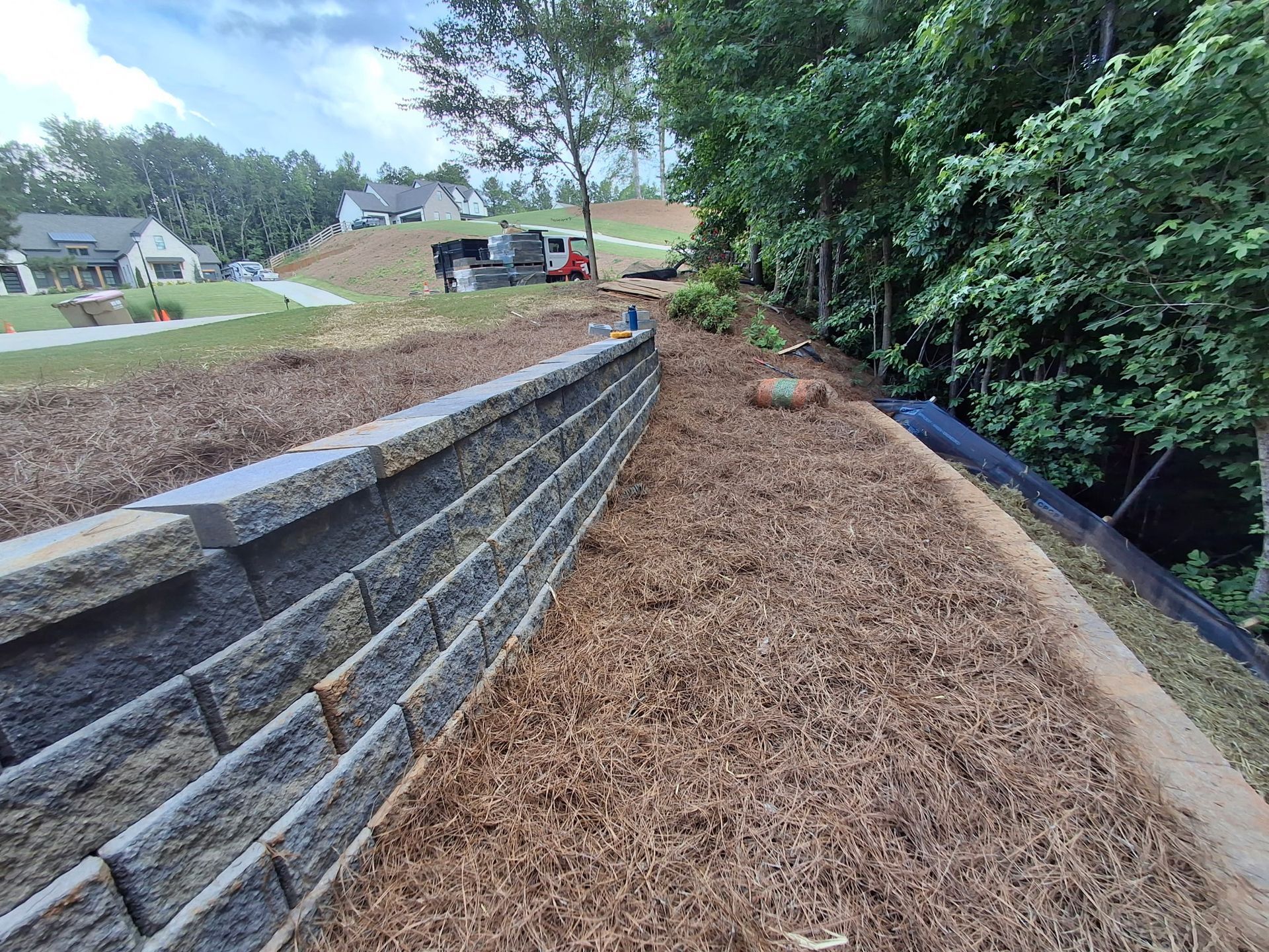 A brick wall is surrounded by mulch and trees on a hillside.