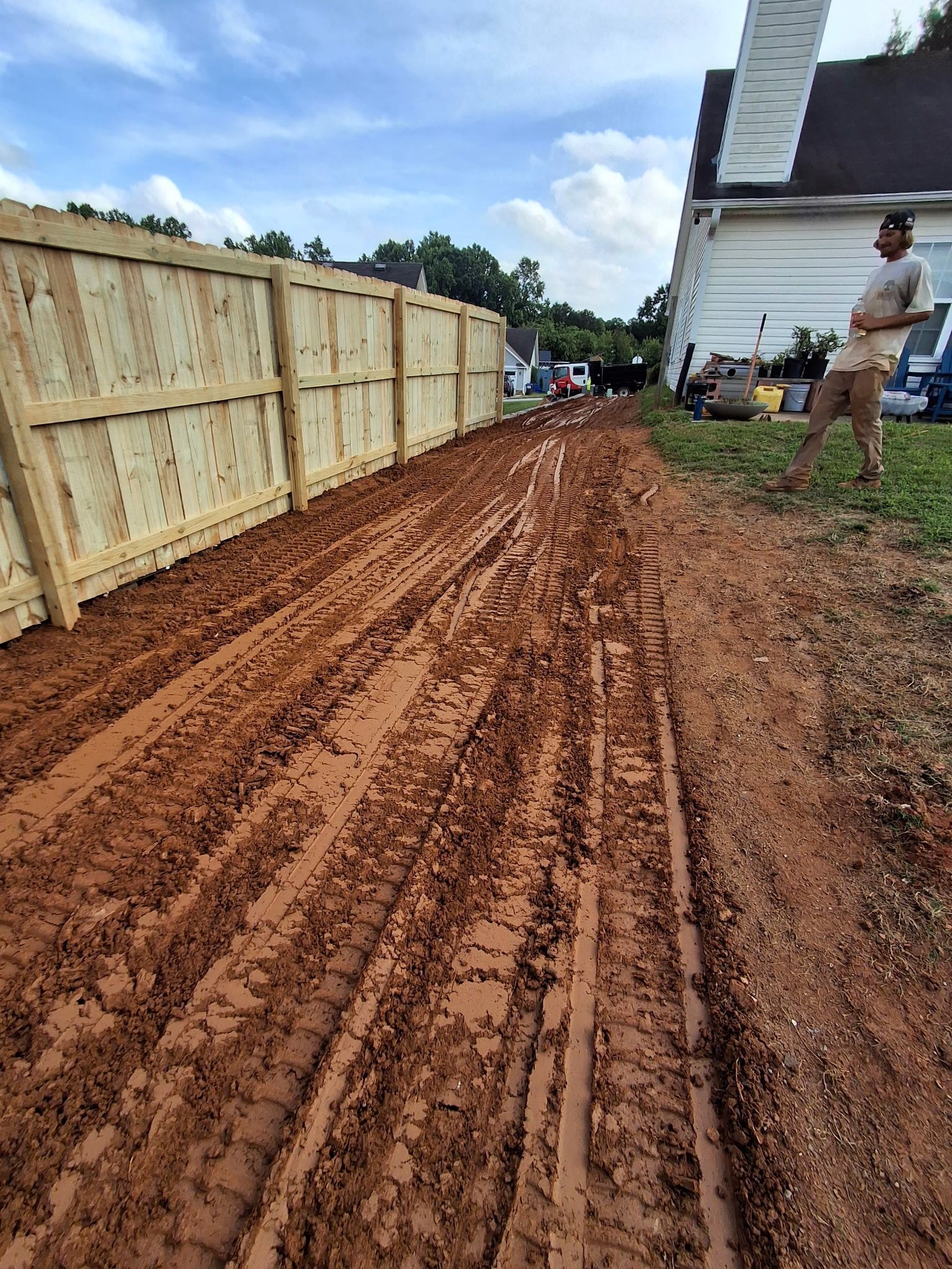 A man is standing on a dirt road next to a wooden fence.