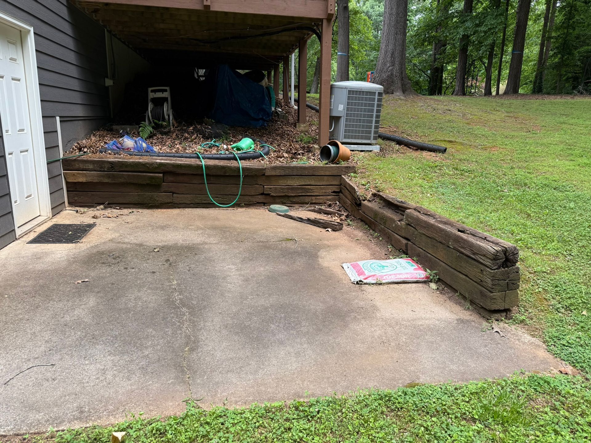 A concrete patio with a wooden wall and a hose in front of a house.
