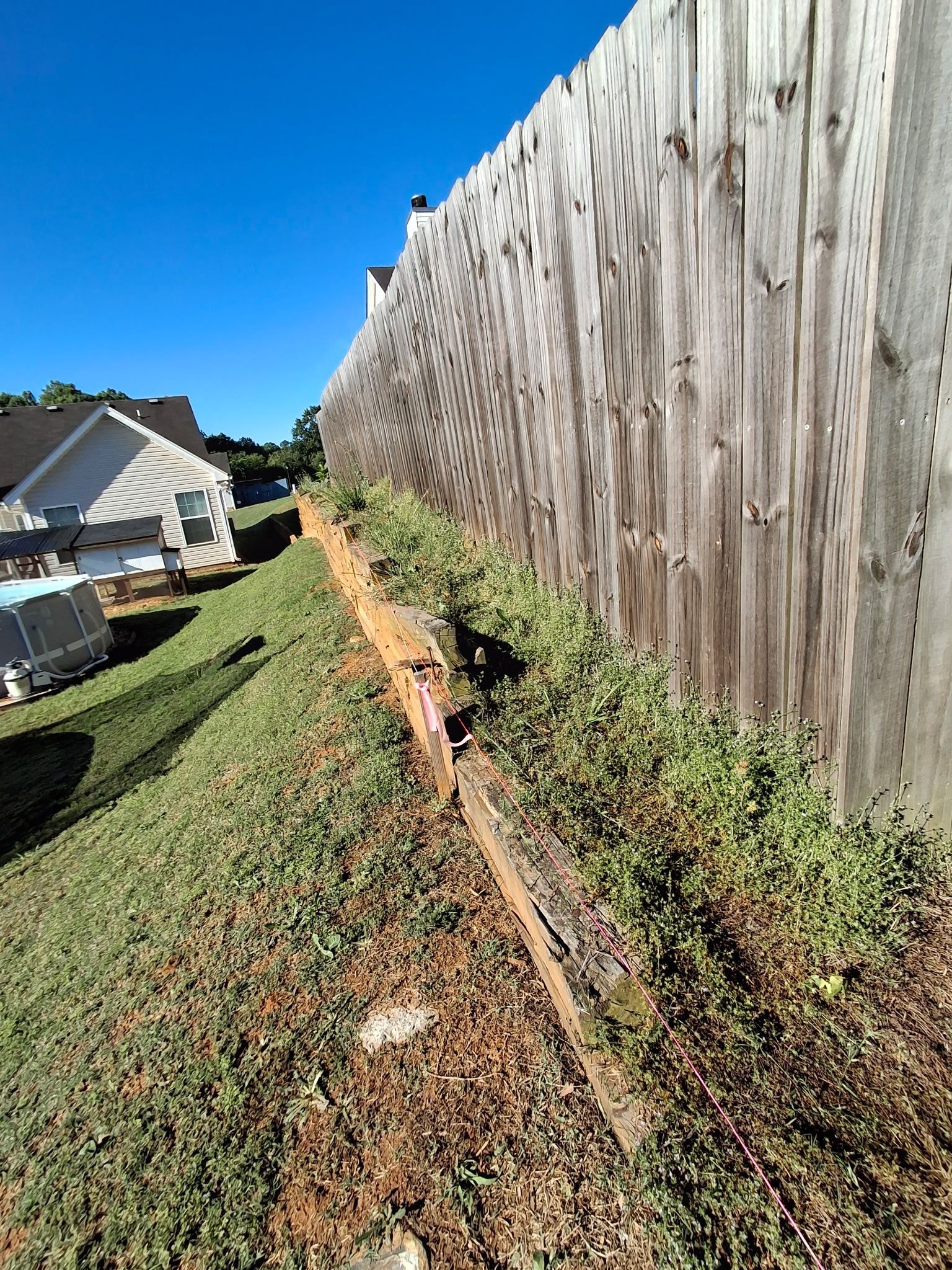 A wooden fence is sitting on top of a grassy hill next to a house.