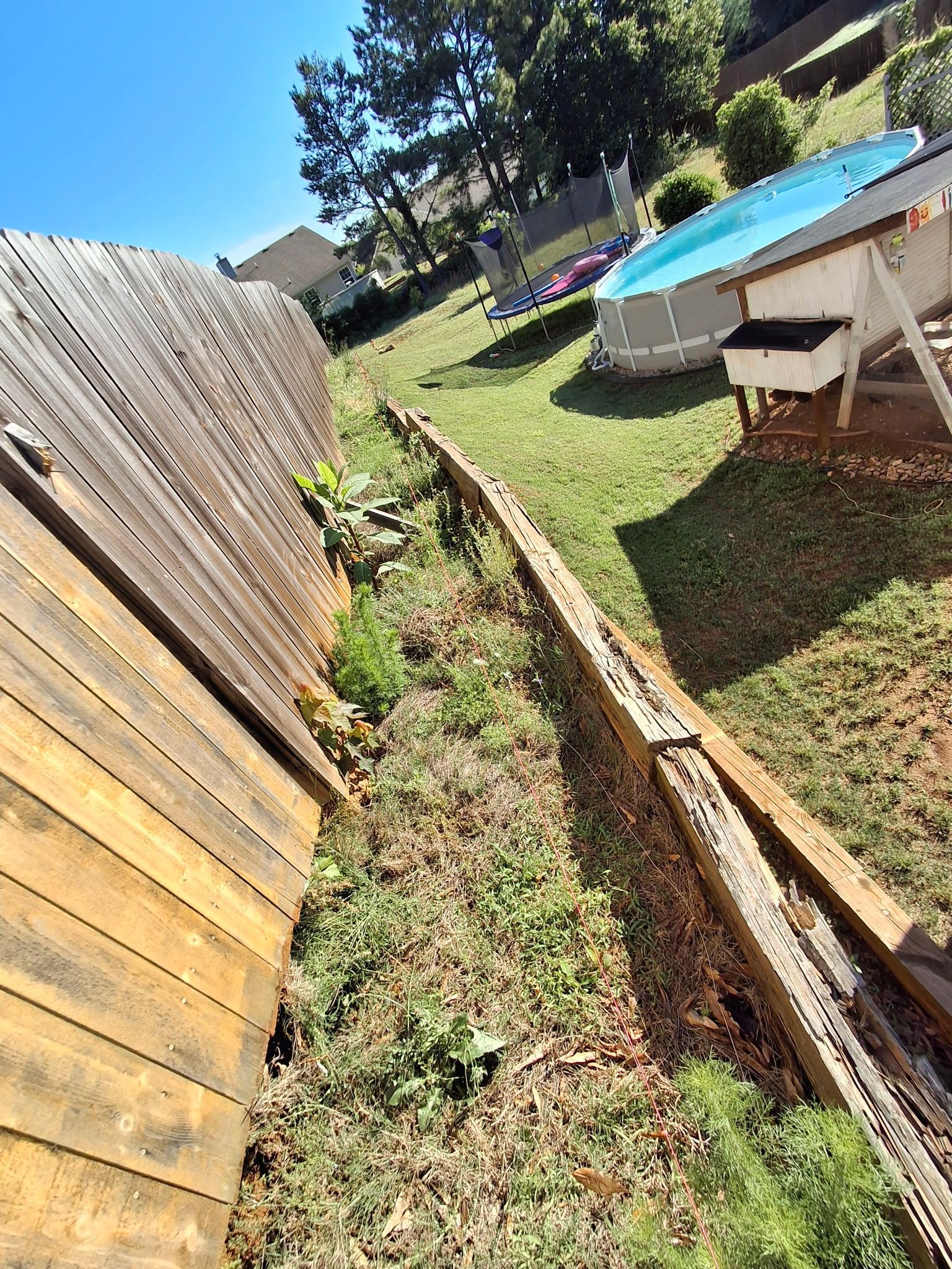 A wooden shed is sitting on top of a grassy hill next to a pool.
