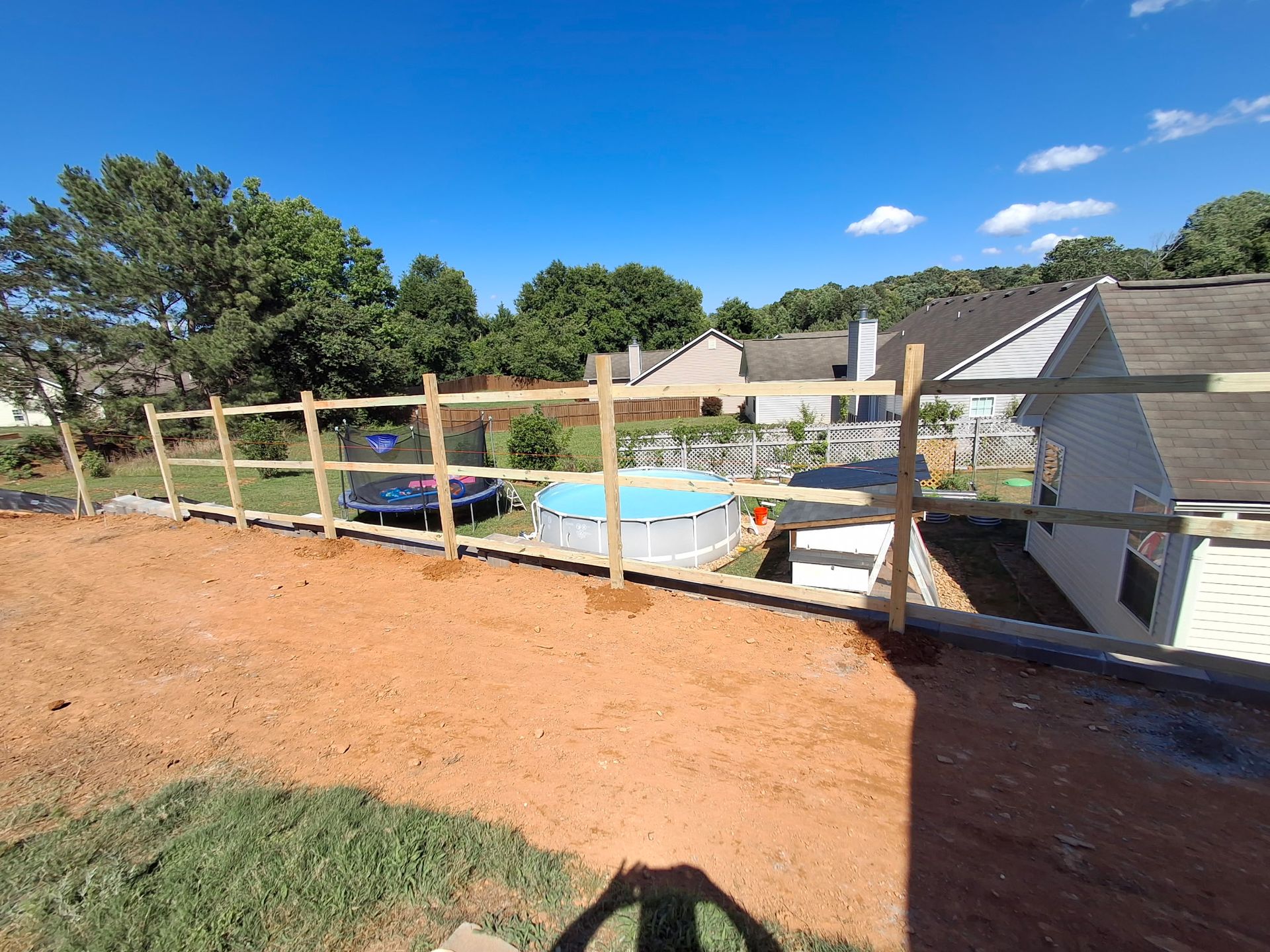 A wooden fence is surrounding a pool in a backyard.