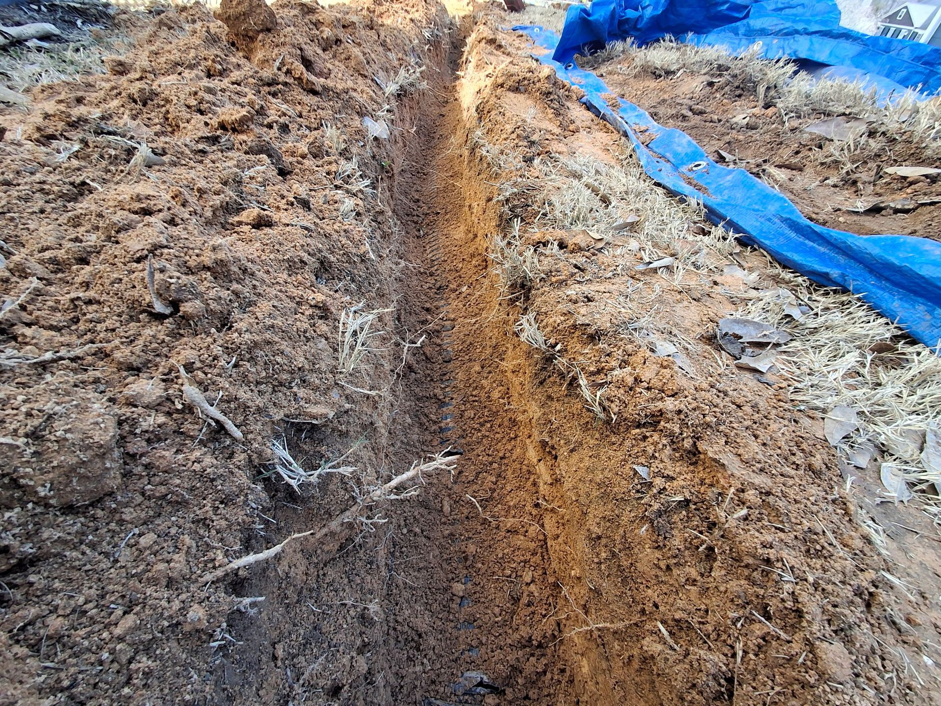 A trench in the dirt with a blue tarp in the background.