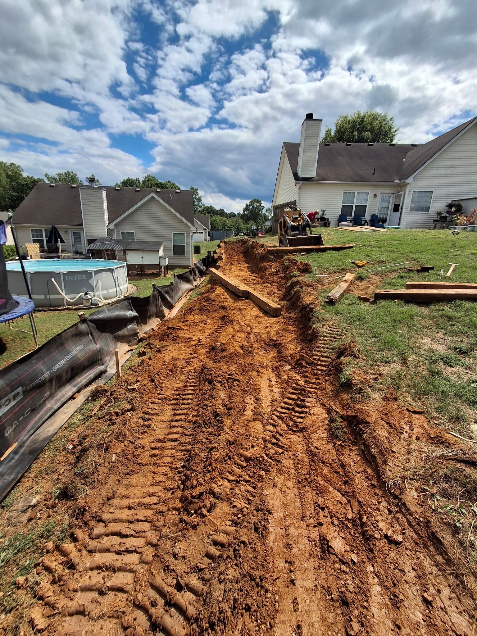 A dirt road leading to a house with a pool in the background.