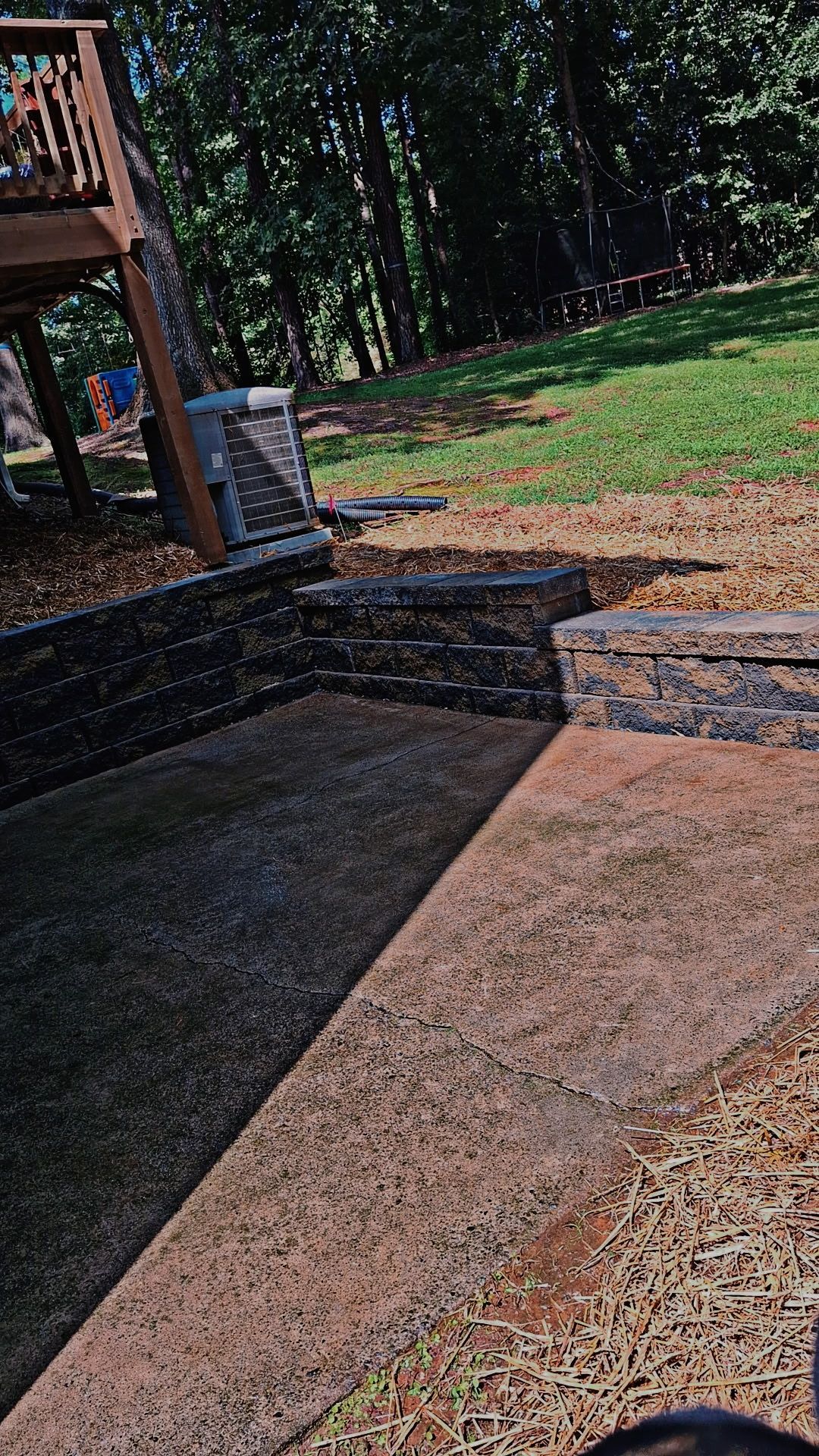 A person is standing on a sidewalk next to a stone wall in a backyard.