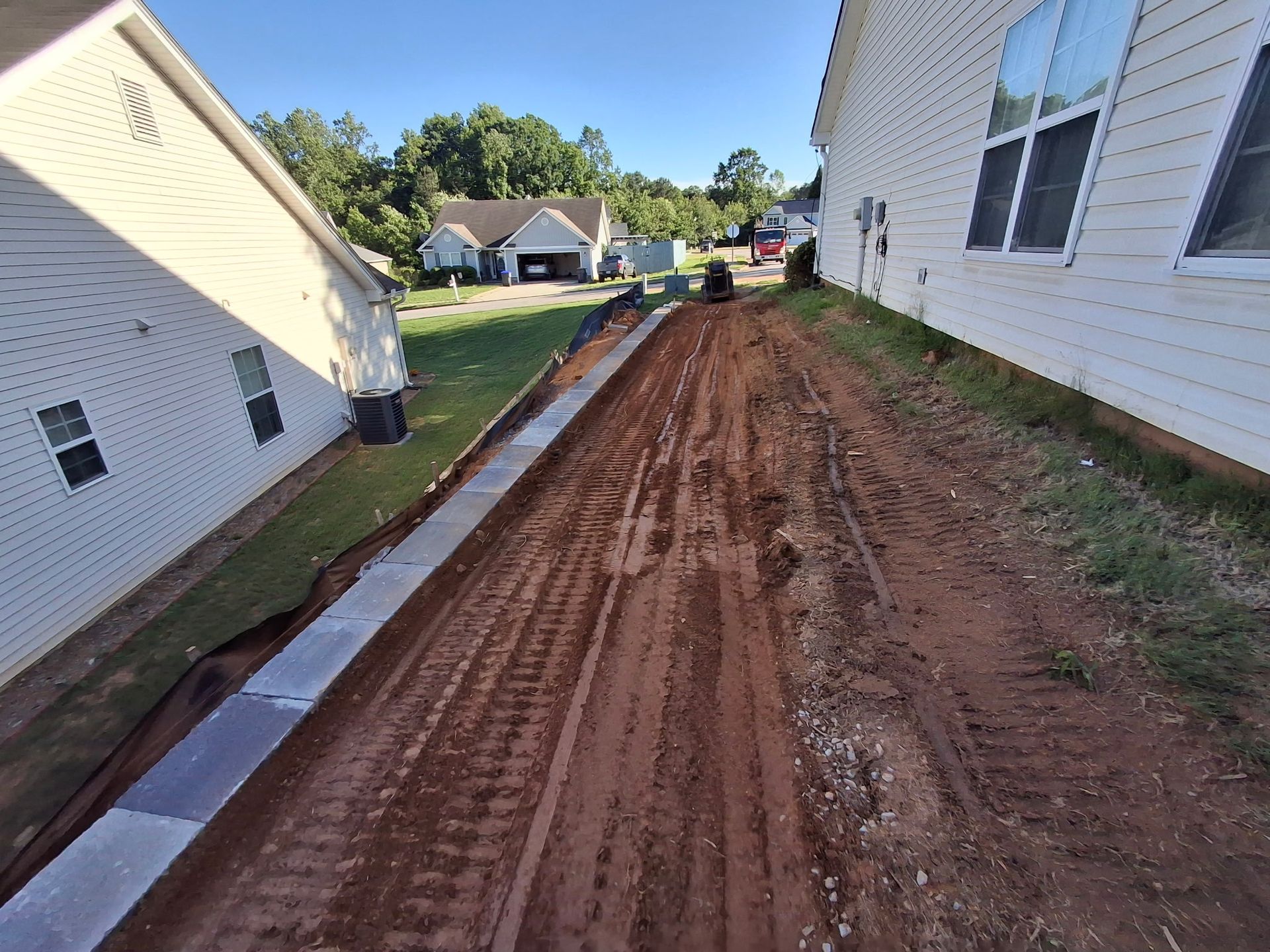 A dirt road leading to a house with a white house in the background.