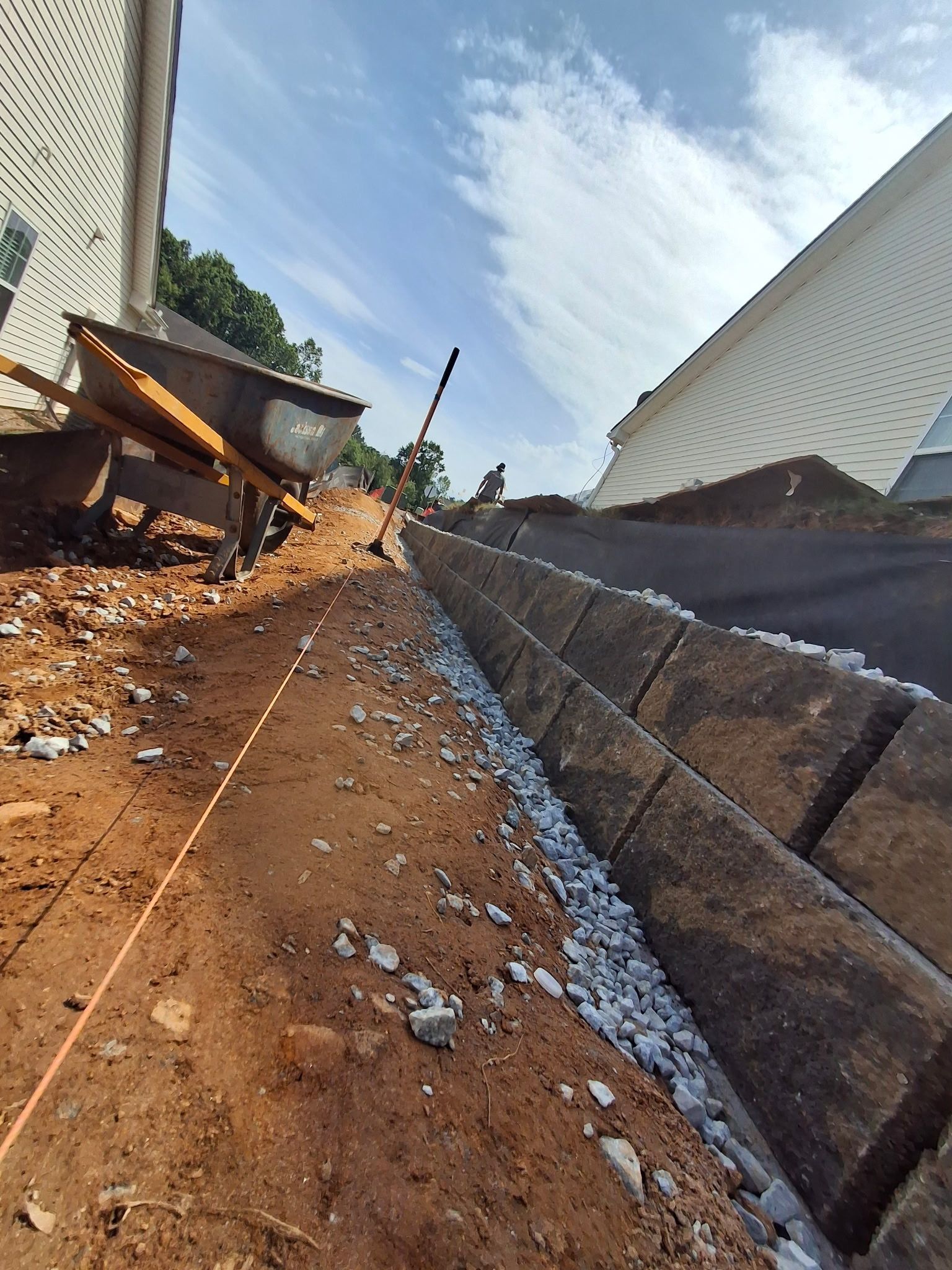 A wheelbarrow is sitting on top of a dirt hill next to a brick wall.