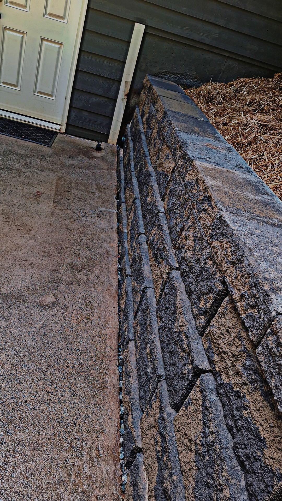 A brick wall is sitting next to a door in front of a house.
