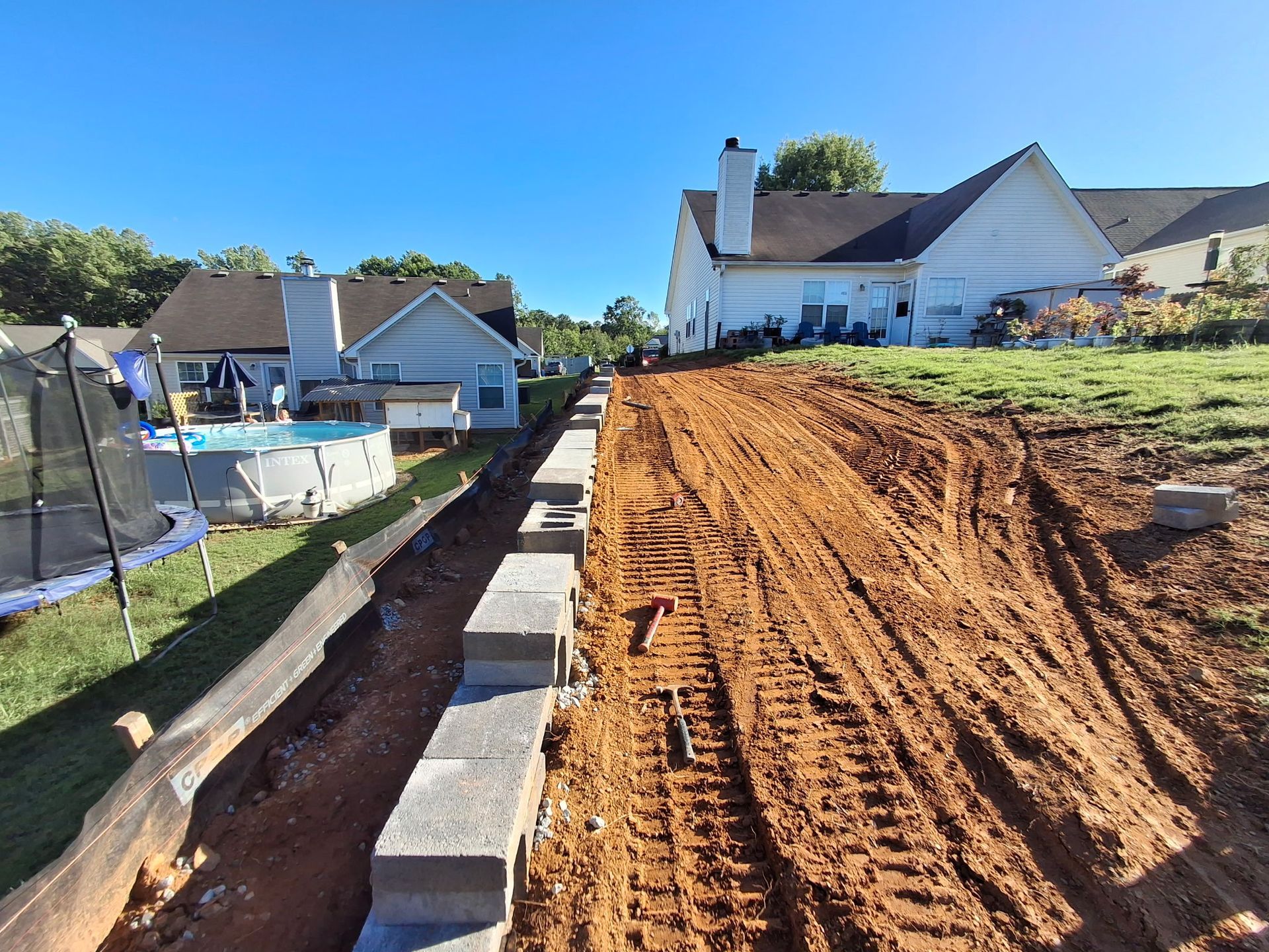 A dirt road leading to a house with a pool in the background.