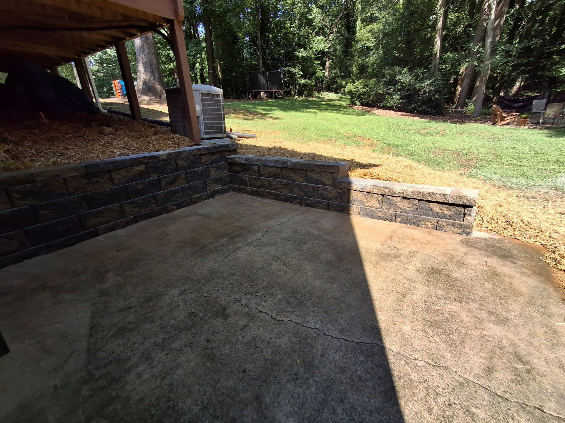 A concrete patio with a stone wall in the backyard of a house.