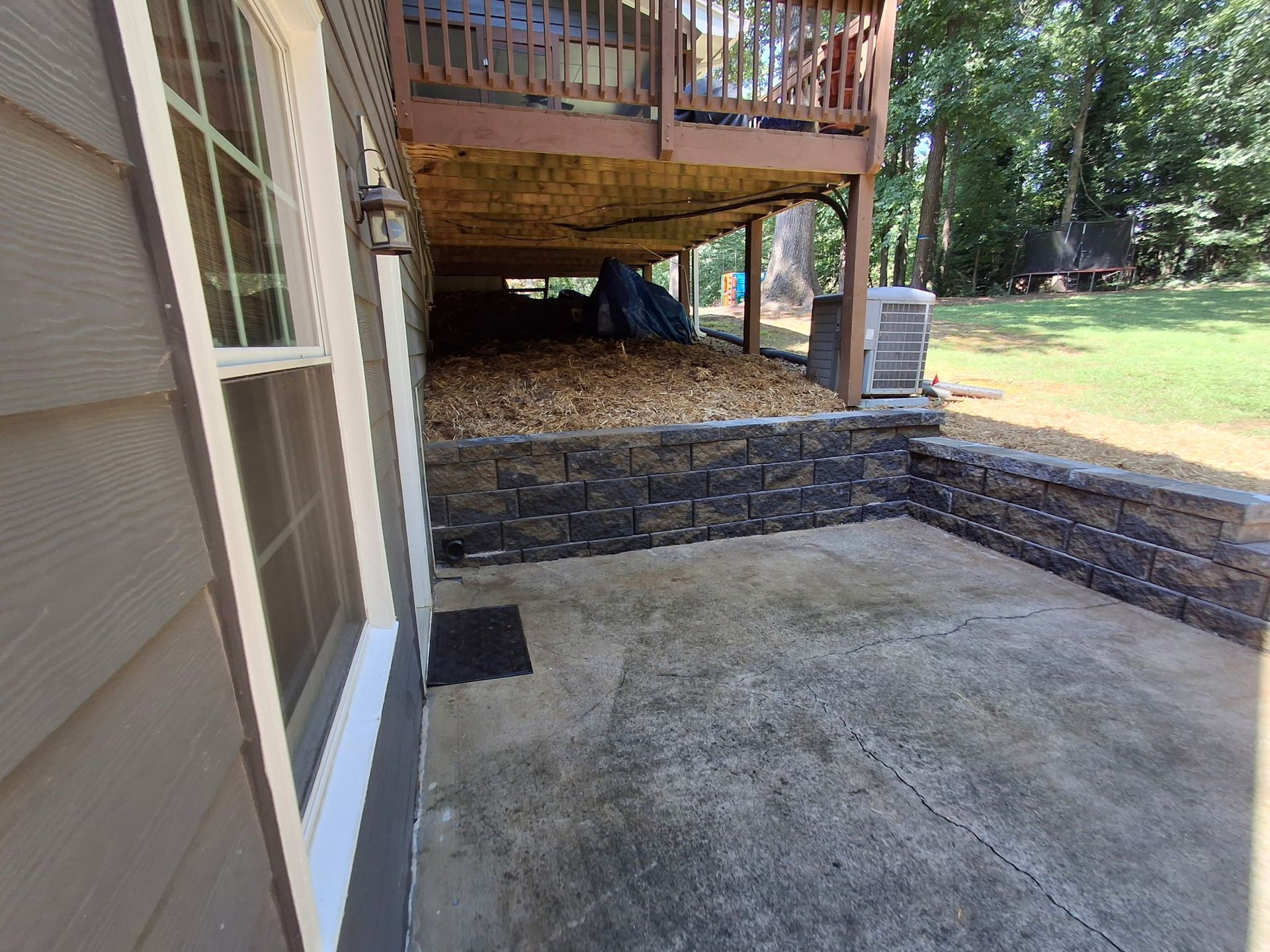 A patio with a deck and a stone wall next to a house.