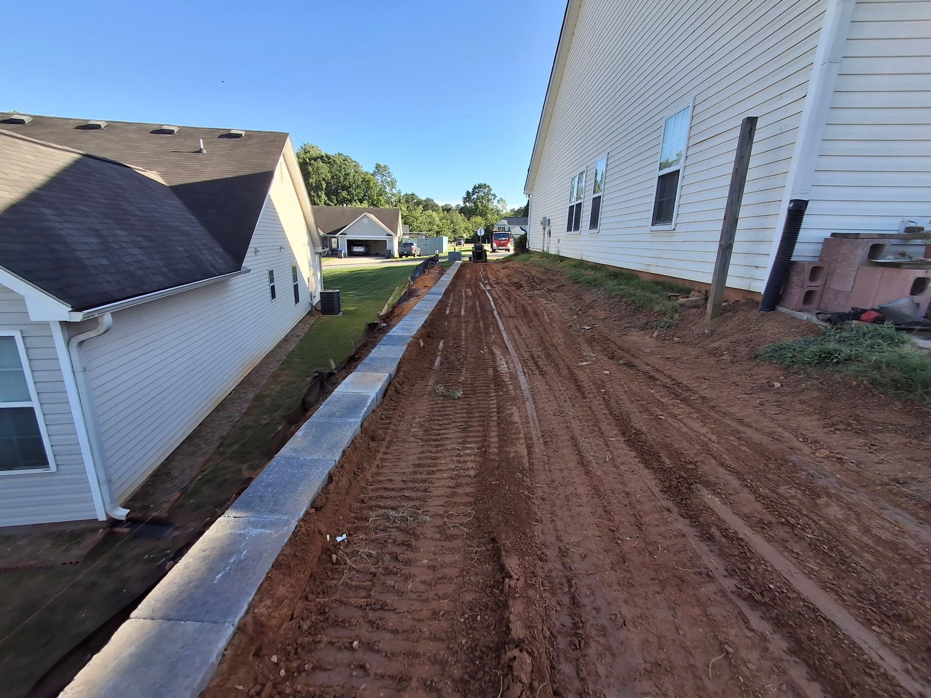 A dirt road between two houses in a residential area.