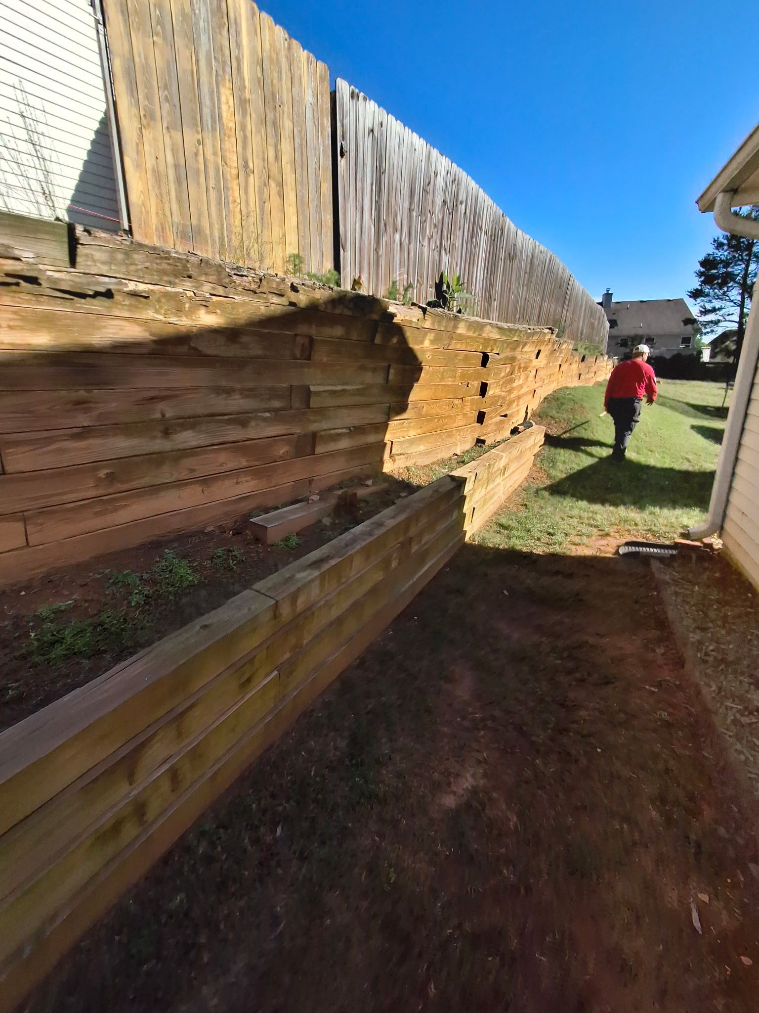 A woman in a red jacket is walking along a wooden fence.