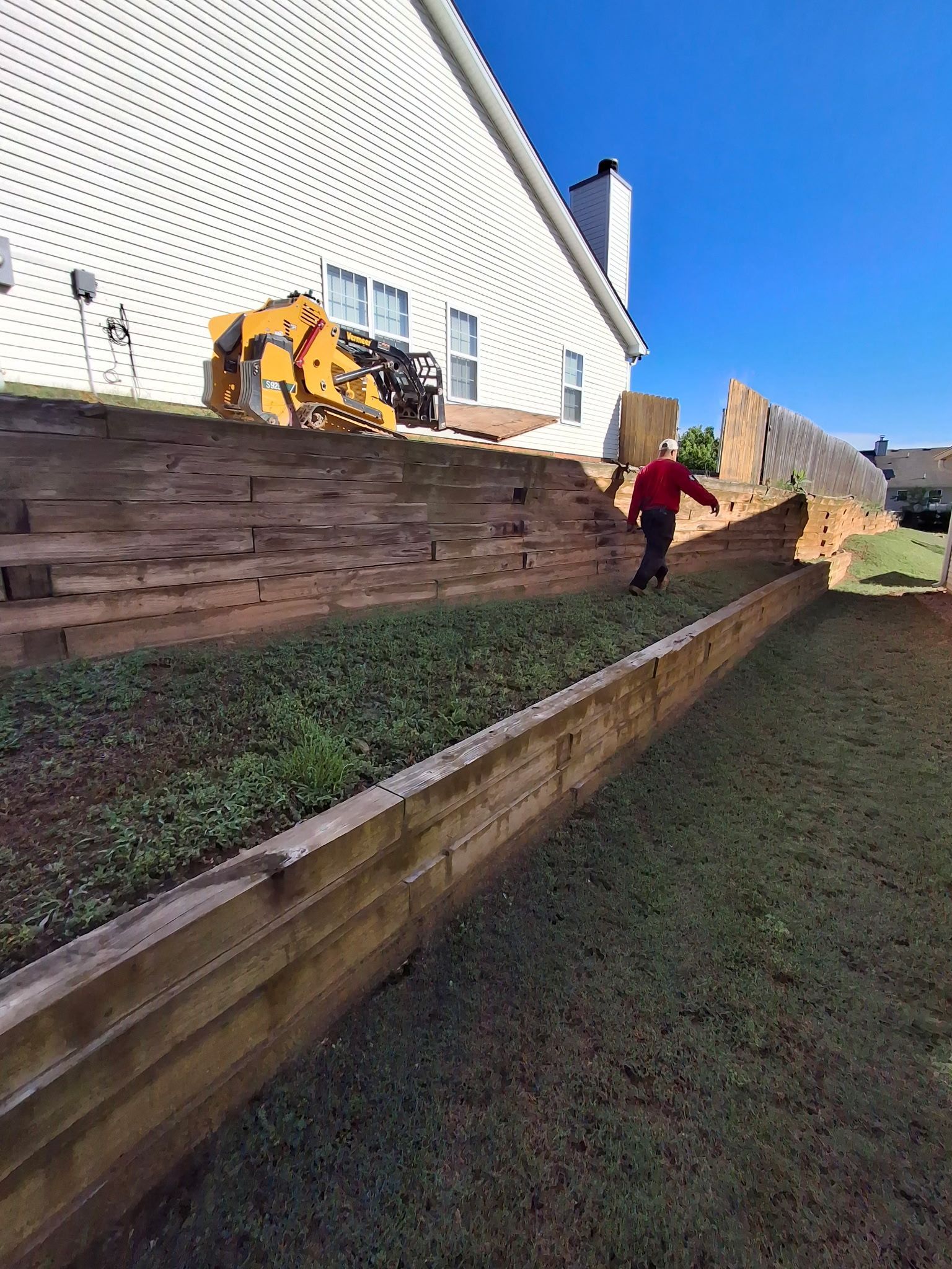 A man is standing next to a wooden wall in front of a house.