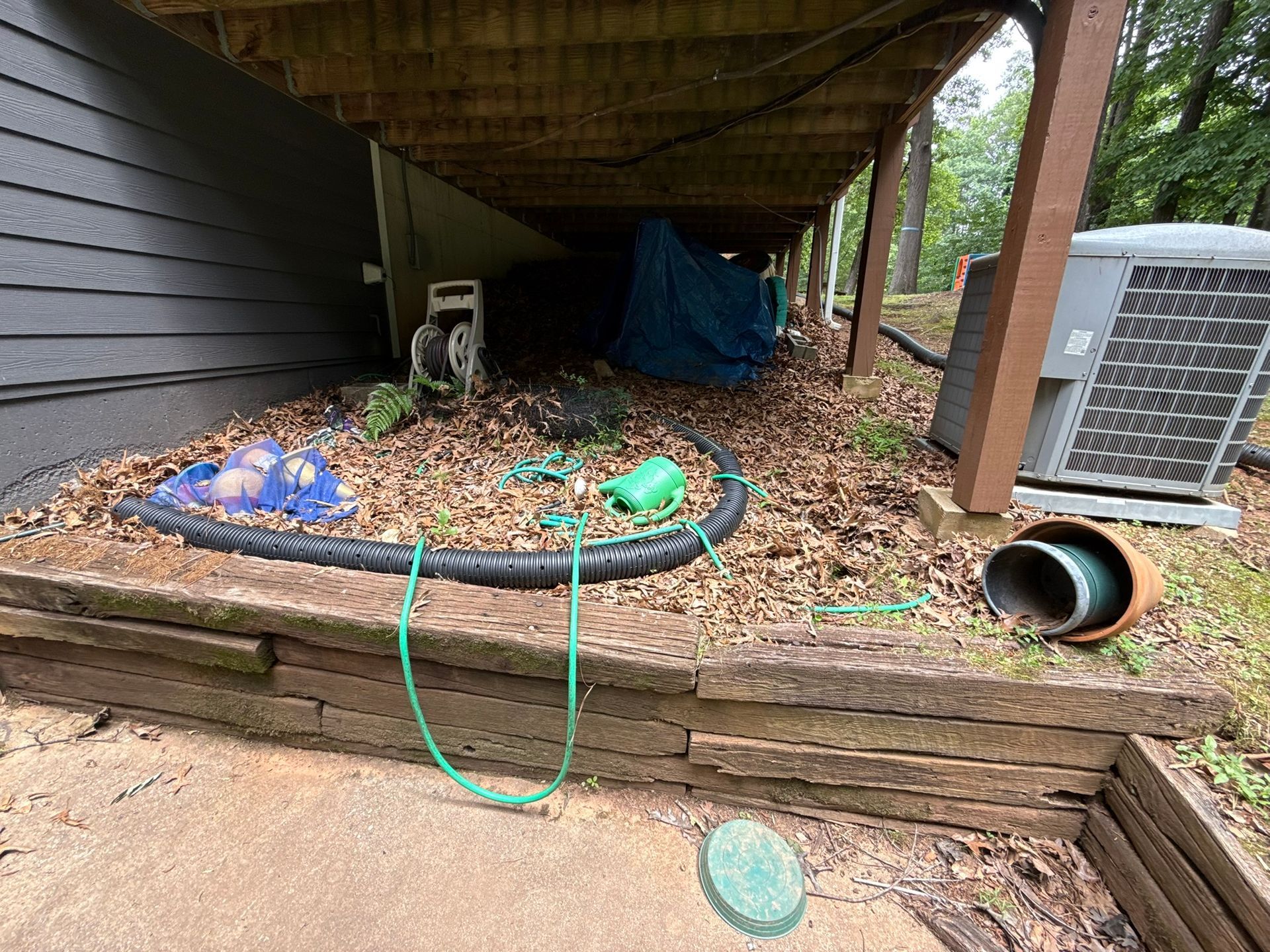 A green hose is connected to a house under a deck.