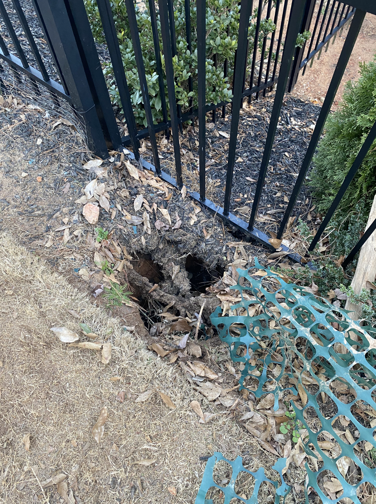There is a hole in the ground next to a fence.