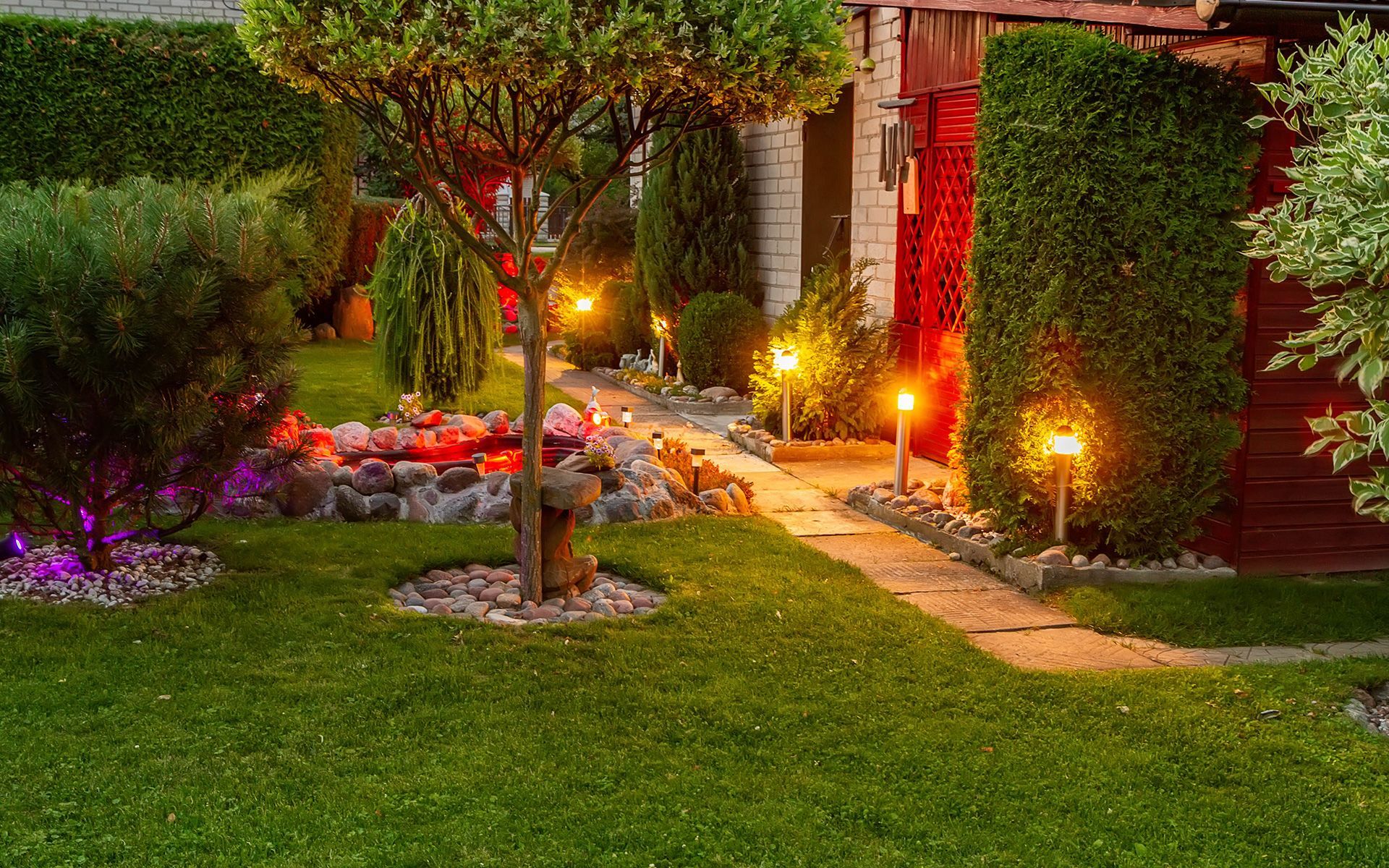 A lush green yard with a path leading to a house at night.