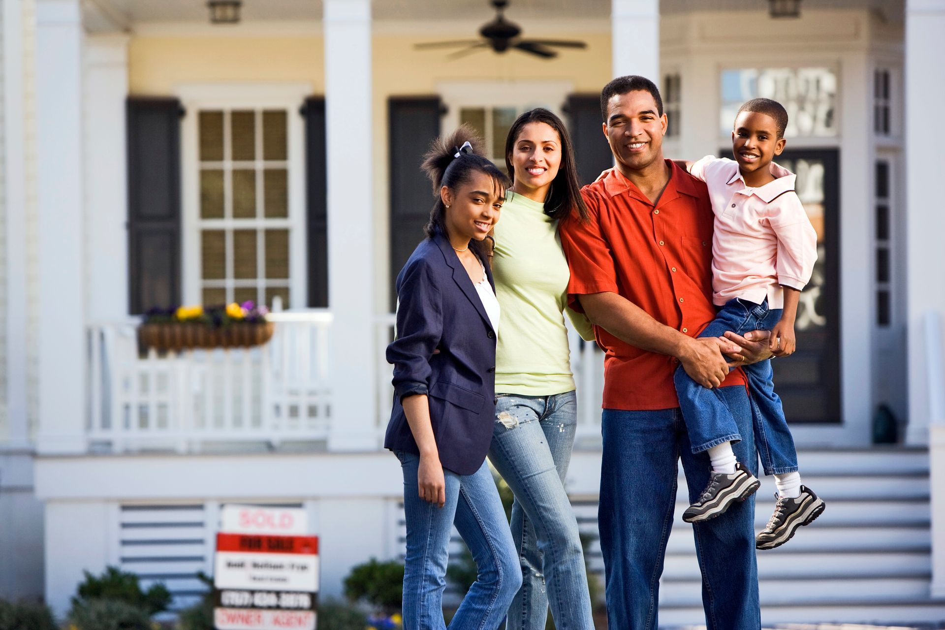 Family of four smiling in front of their new home. Father holding child.