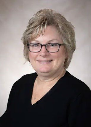 Woman with short blonde hair, glasses, and black shirt smiles at camera.