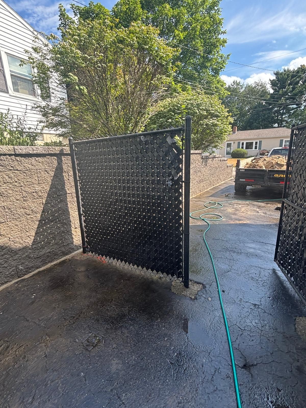 Black privacy fence with a patterned design in a driveway. A garden hose is on the pavement.