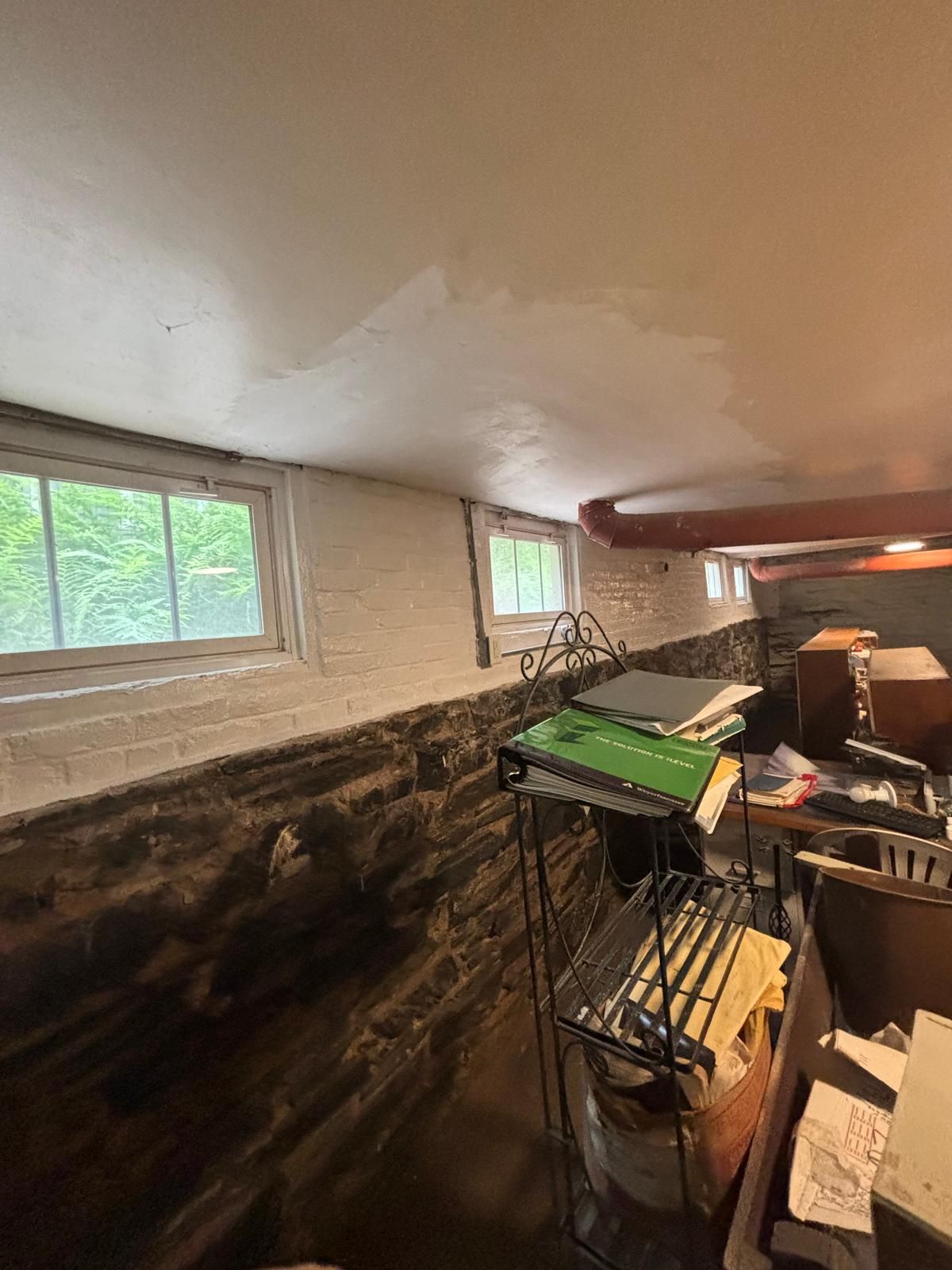 Basement interior with stone wall, white painted walls, small windows, and clutter in the foreground.