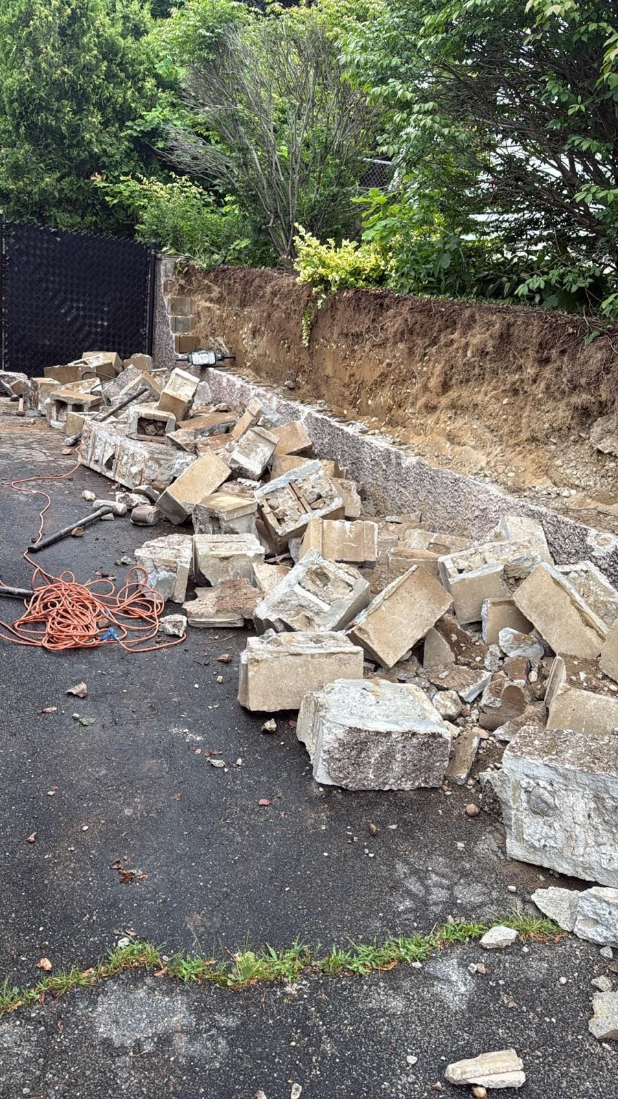 Debris from a demolished stone wall on a paved surface, with an exposed earth embankment behind.