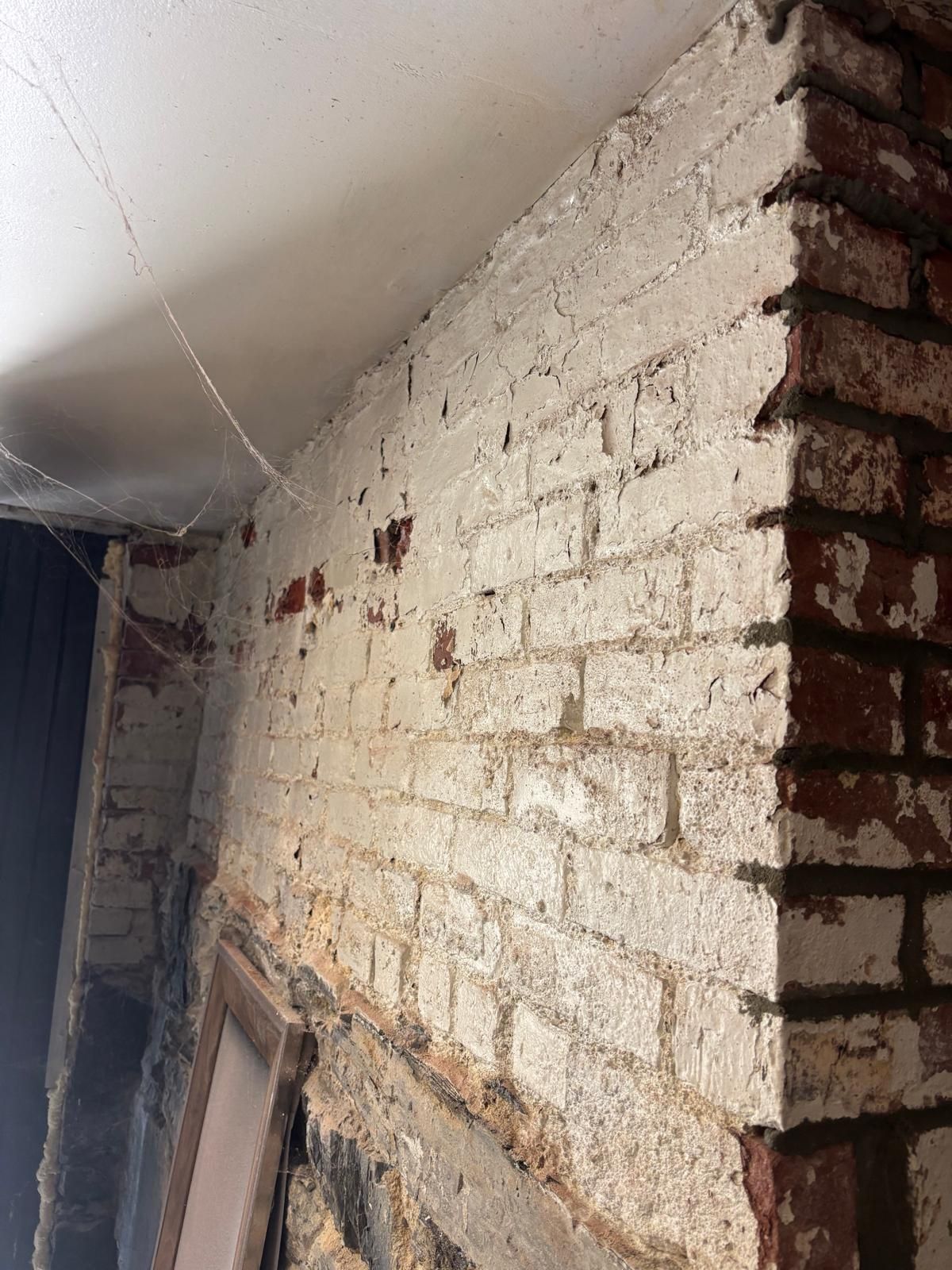 Brick wall, partially painted white, meets a ceiling. Corner shows red brick.