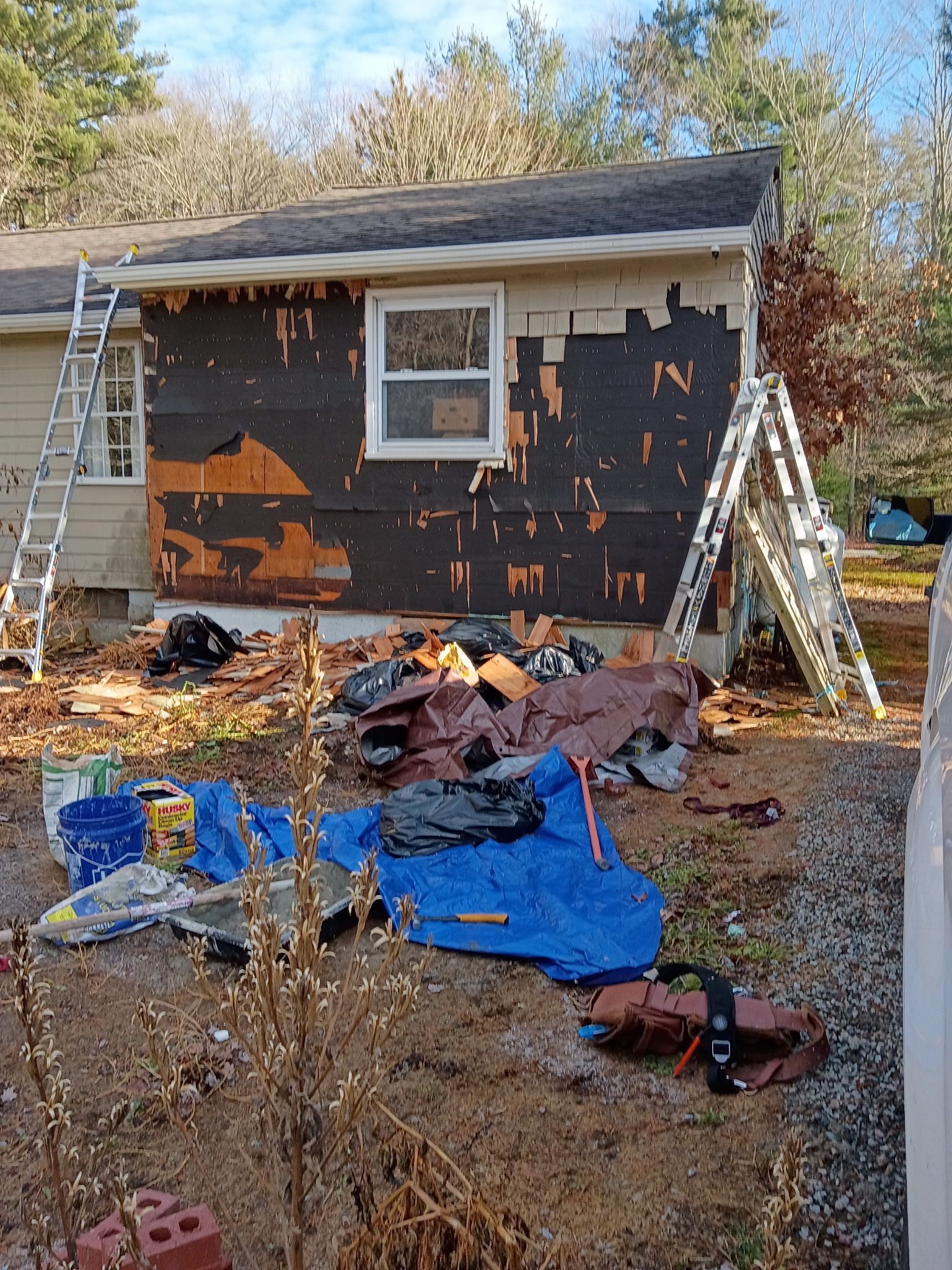 House exterior under construction, exposed sheathing, ladders, and debris visible.