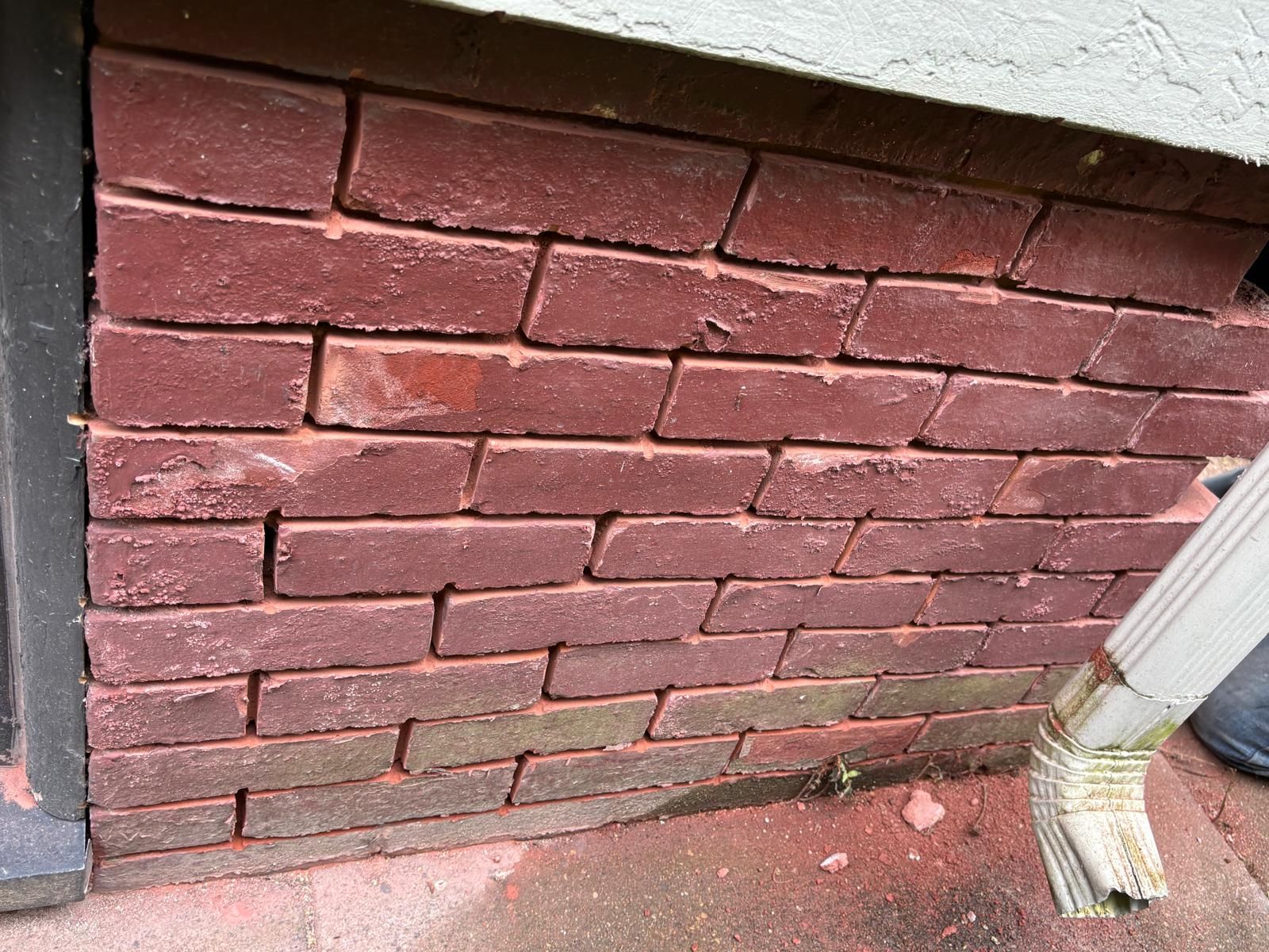 Red brick foundation of a building with visible mortar, beneath a white structure and a downspout.