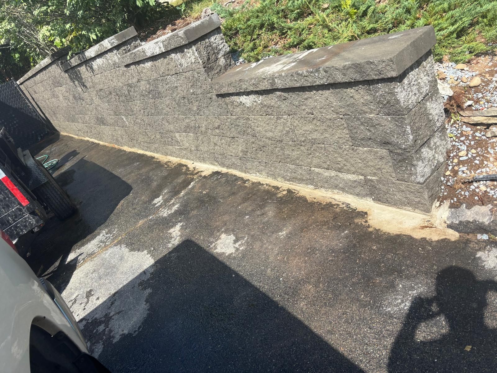 Concrete retaining wall next to paved area, shadowed by a vehicle.