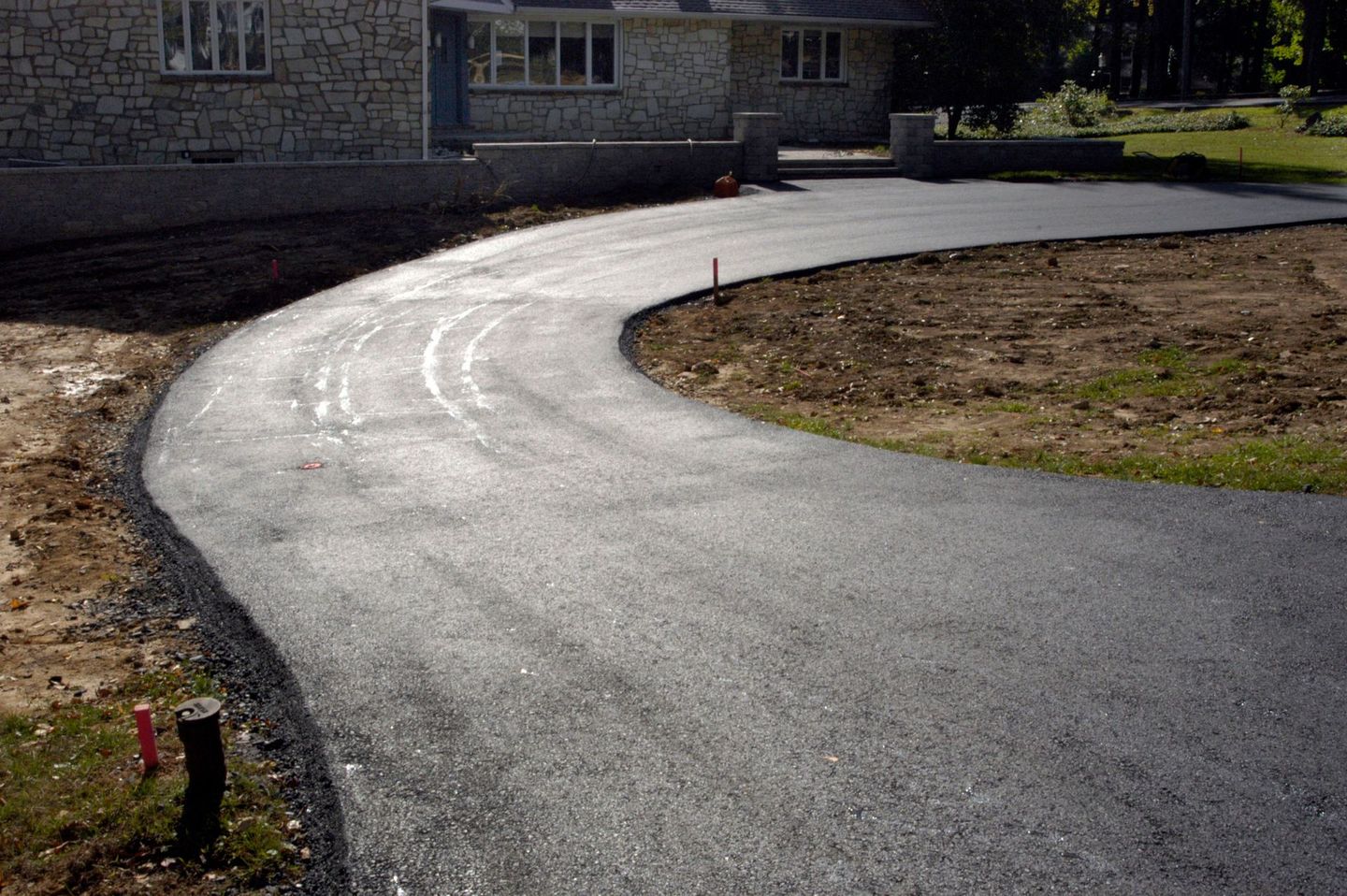 Freshly paved asphalt driveway leading to a stone house with a curved layout