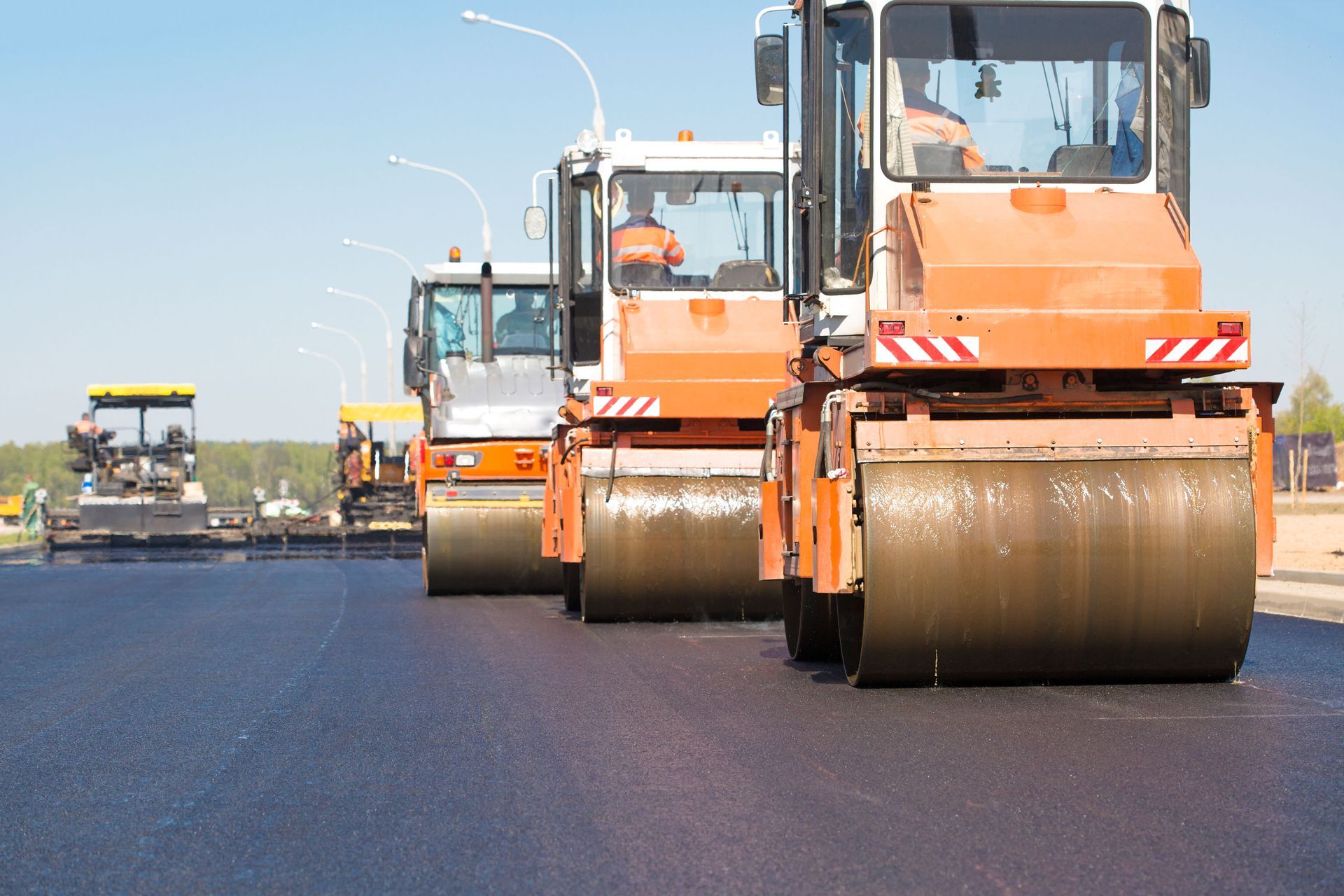 Asphalt rollers in a line rolling down a stamped road.