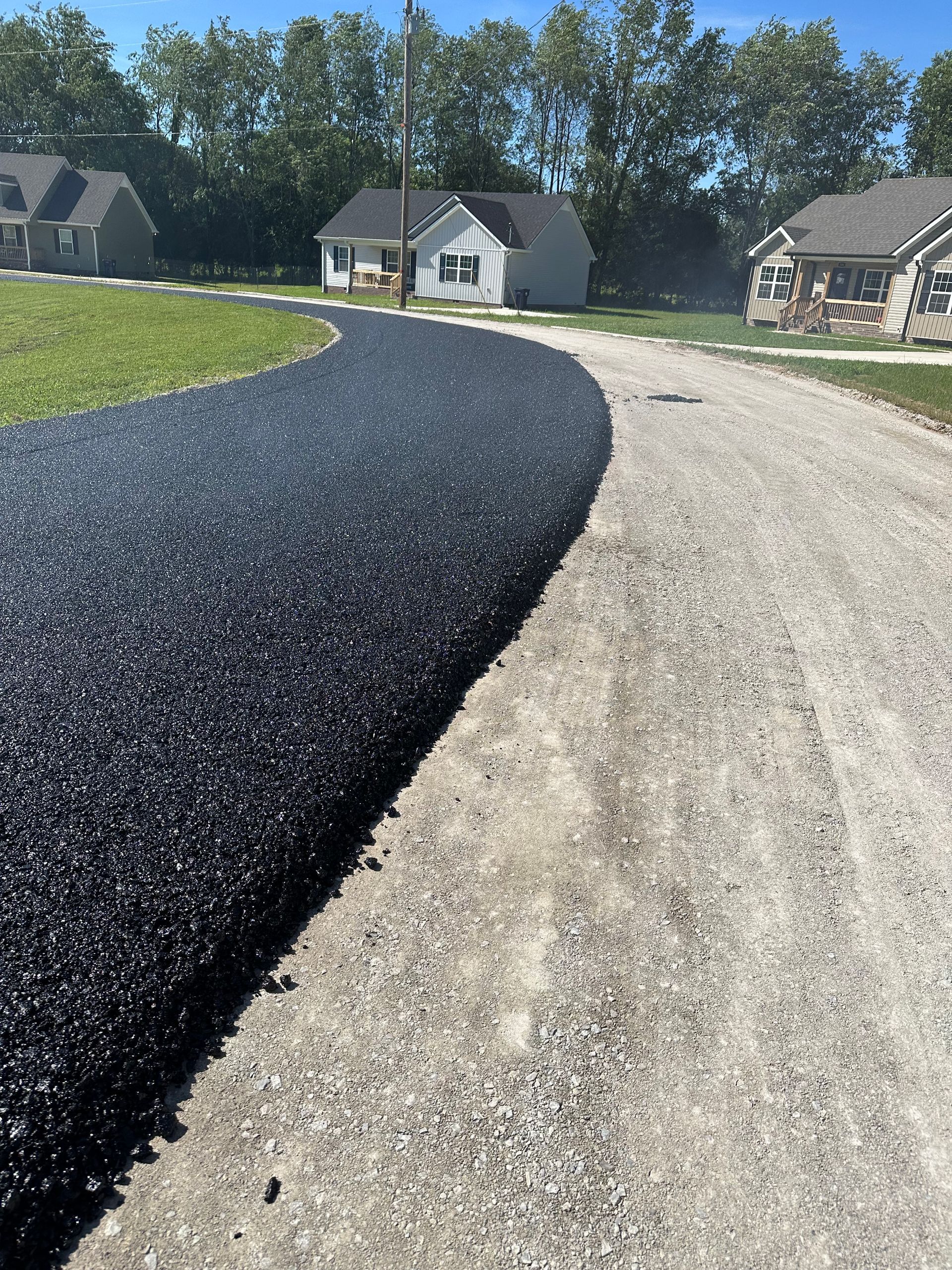 A dirt road going through a residential area with houses in the background.