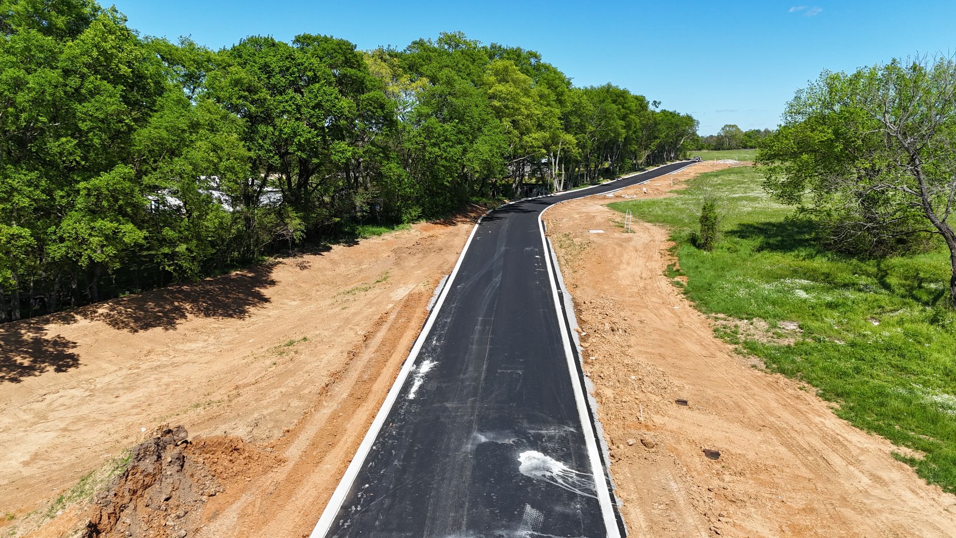 An aerial view of a newly paved road surrounded by trees and dirt.
