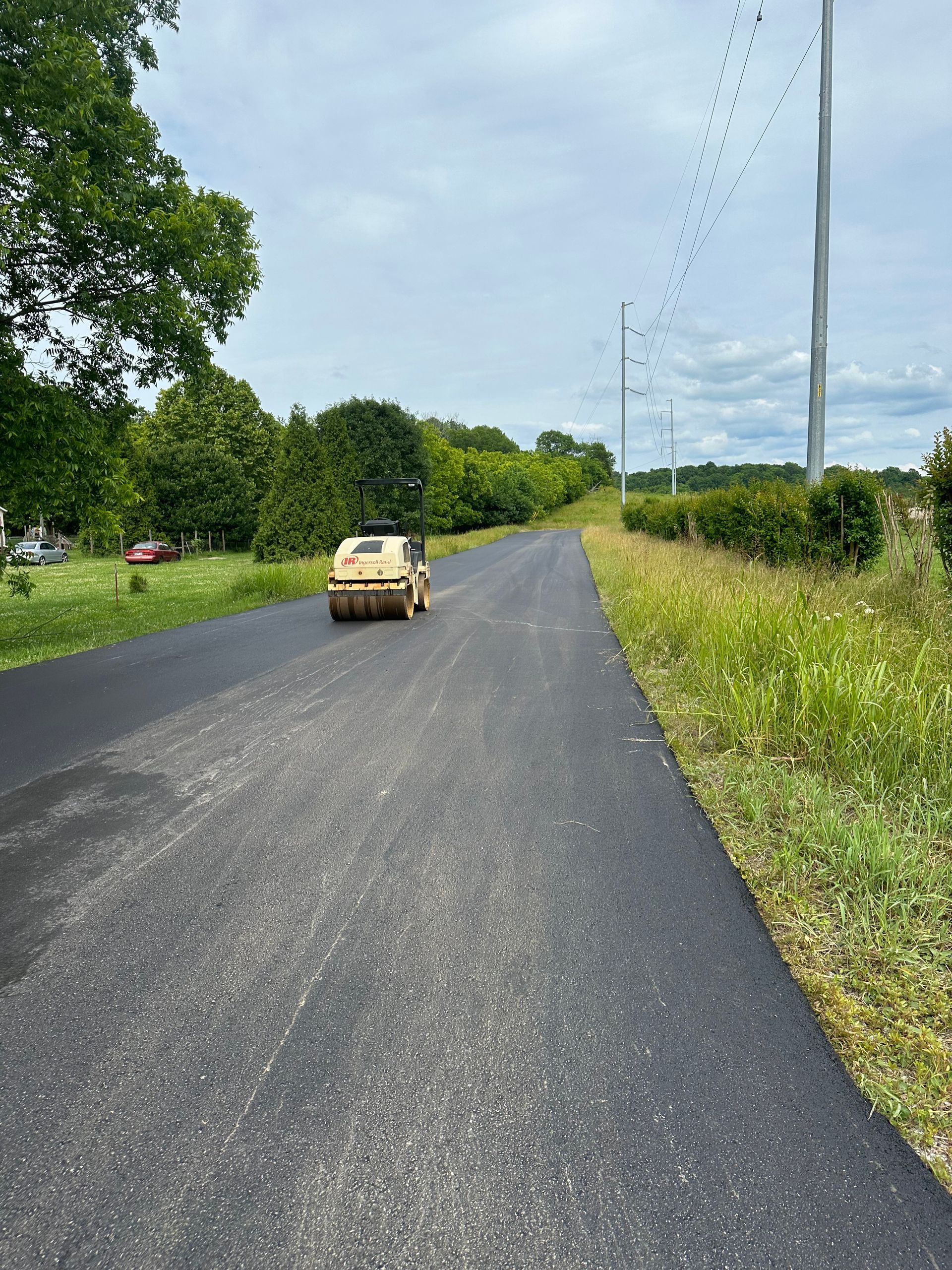 A car is driving down a road next to a grassy field.