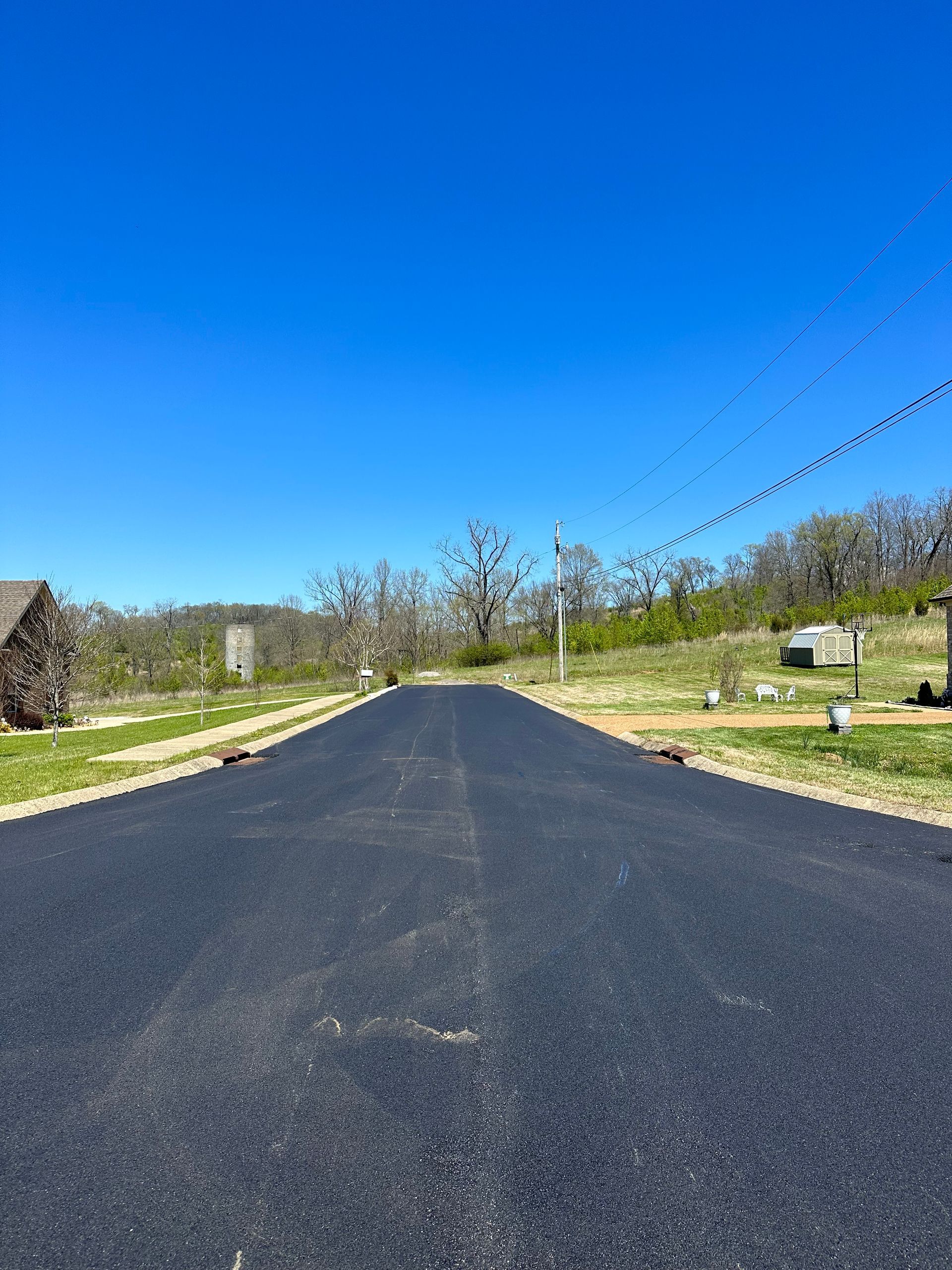 A black asphalt road going through a cemetery on a sunny day.