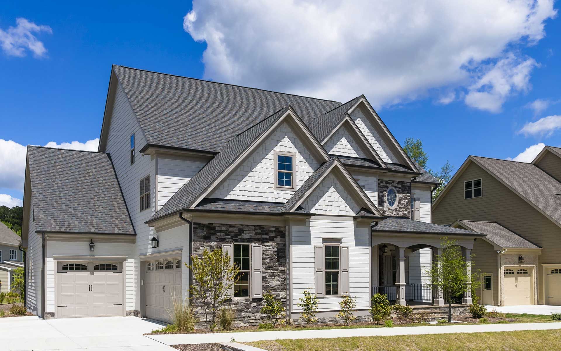 A large white house with a gray roof is sitting on top of a lush green hillside.