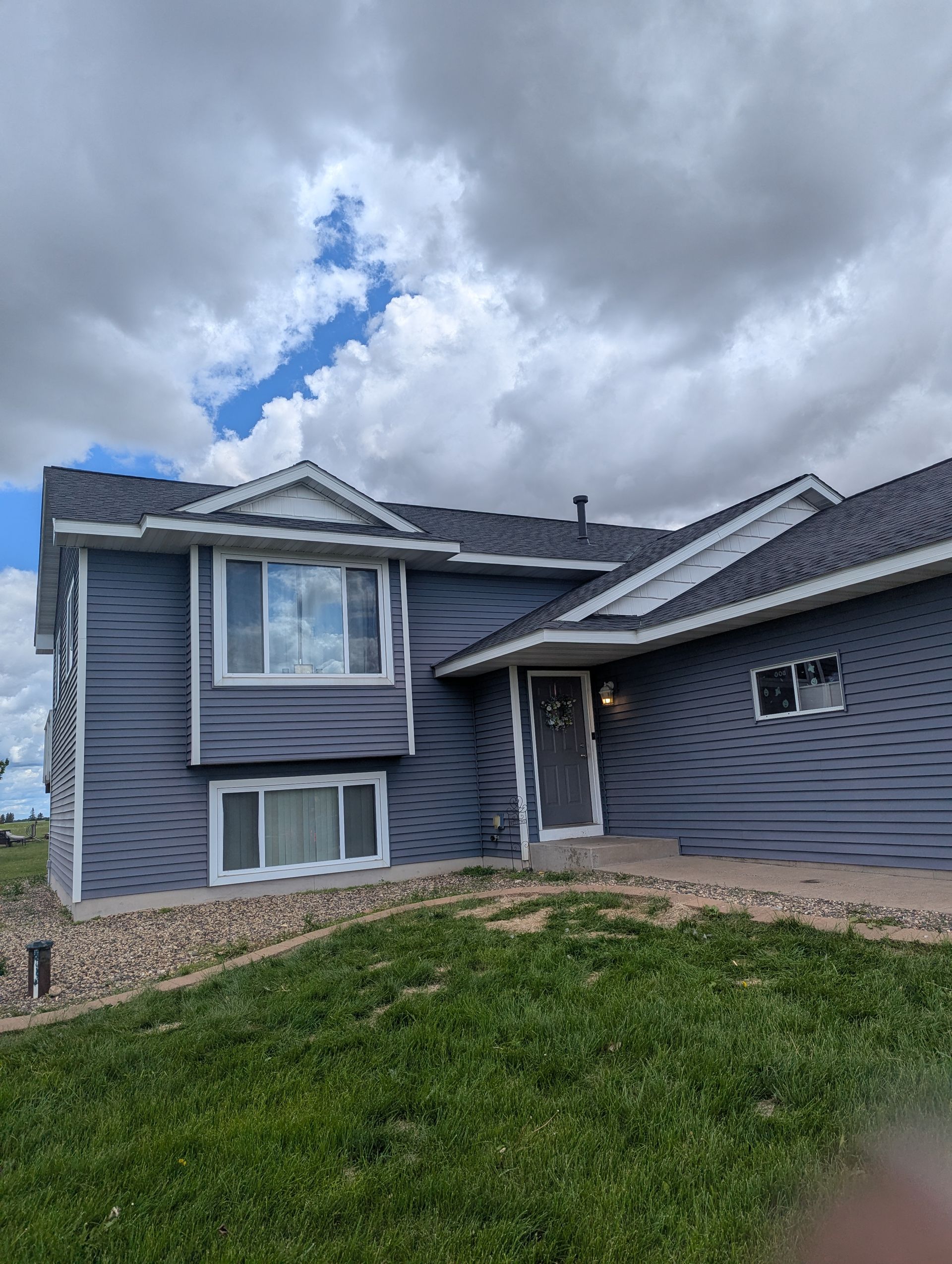A large gray house with a gray roof is sitting on top of a lush green hillside.