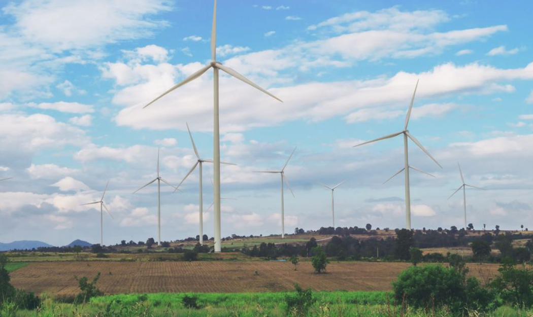 Wind turbines in a rural field under a partly cloudy blue sky.