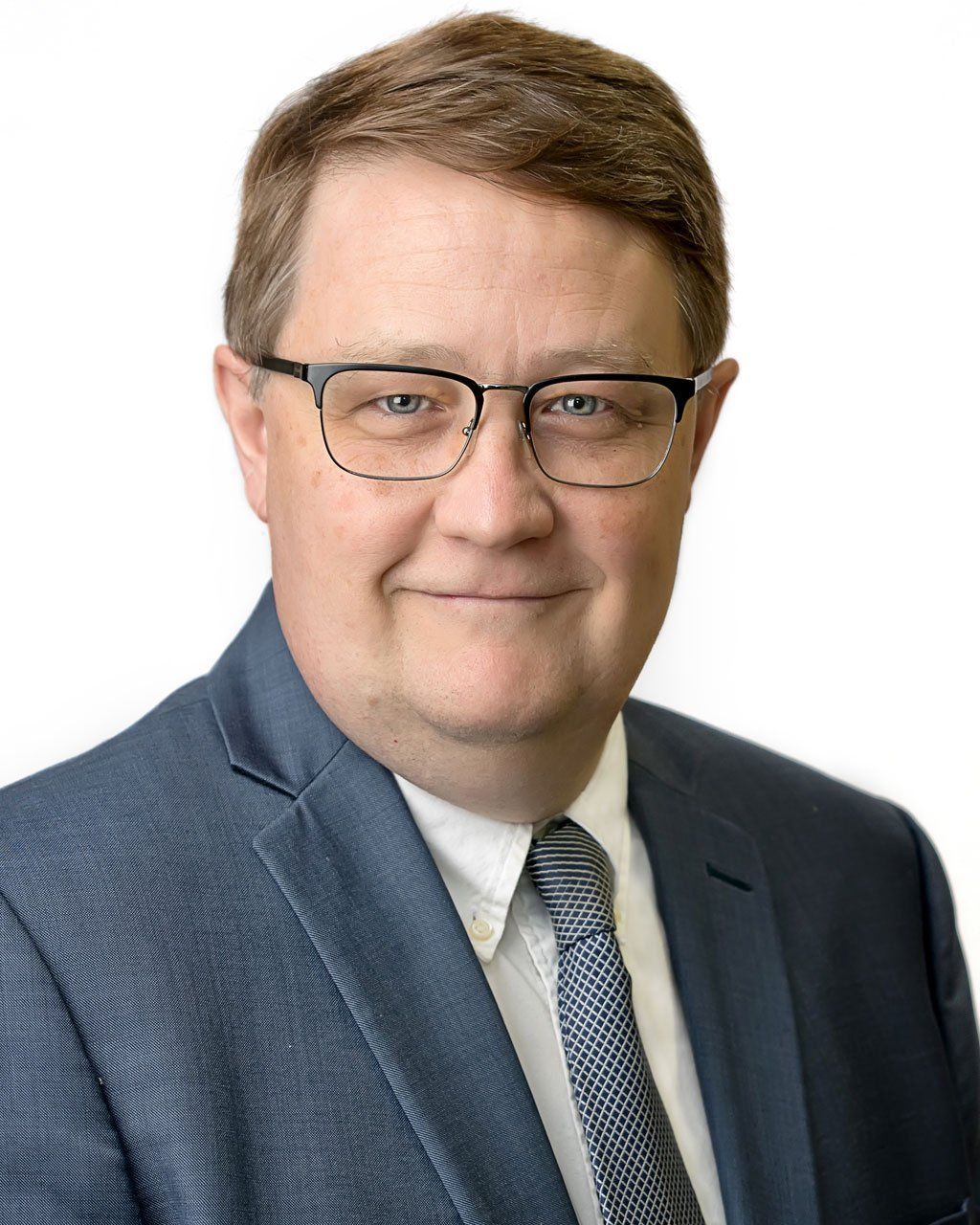 Man in glasses, blue suit, and tie smiling, headshot.