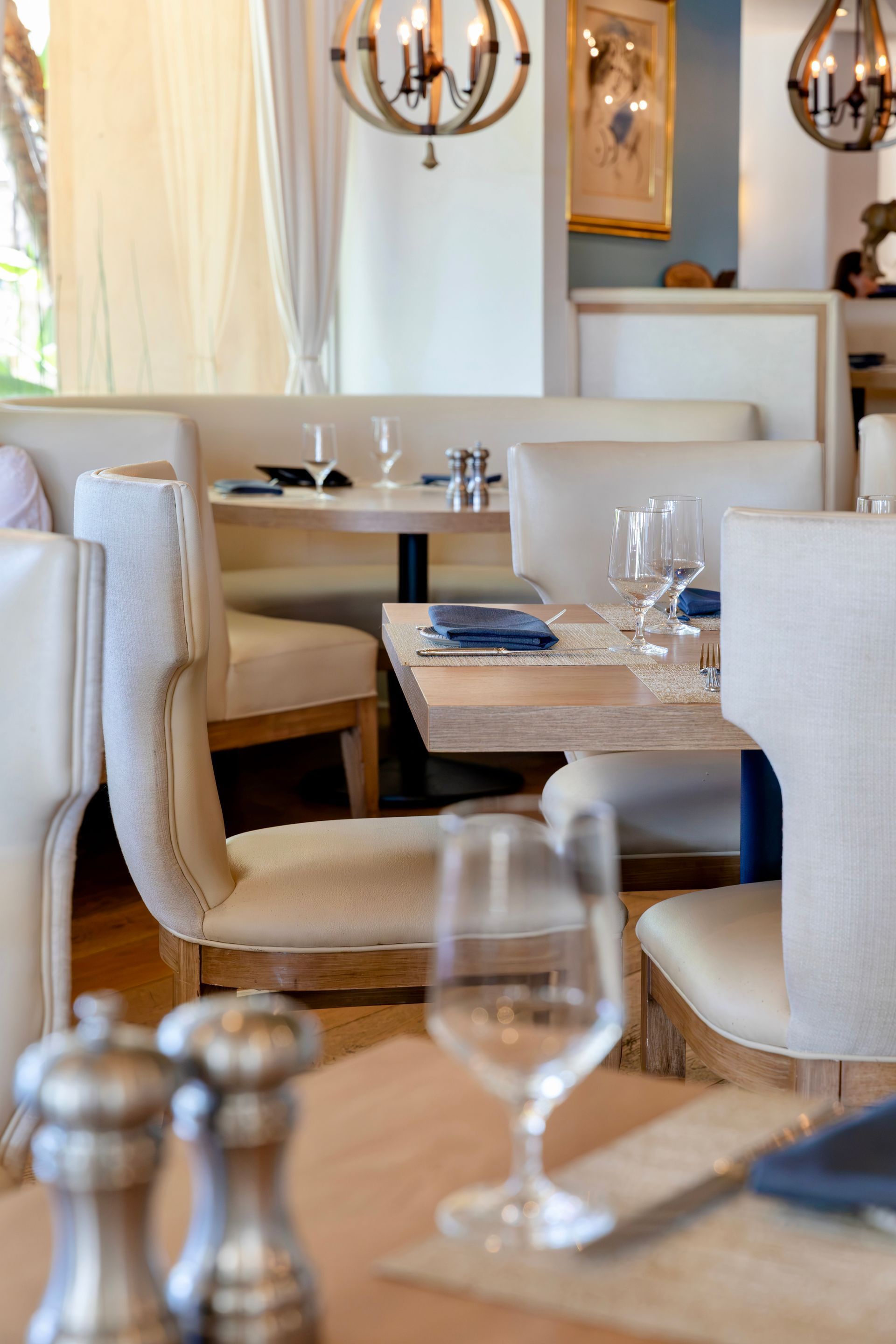 Elegant restaurant dining area with beige chairs, wooden tables, and soft pendant lighting.