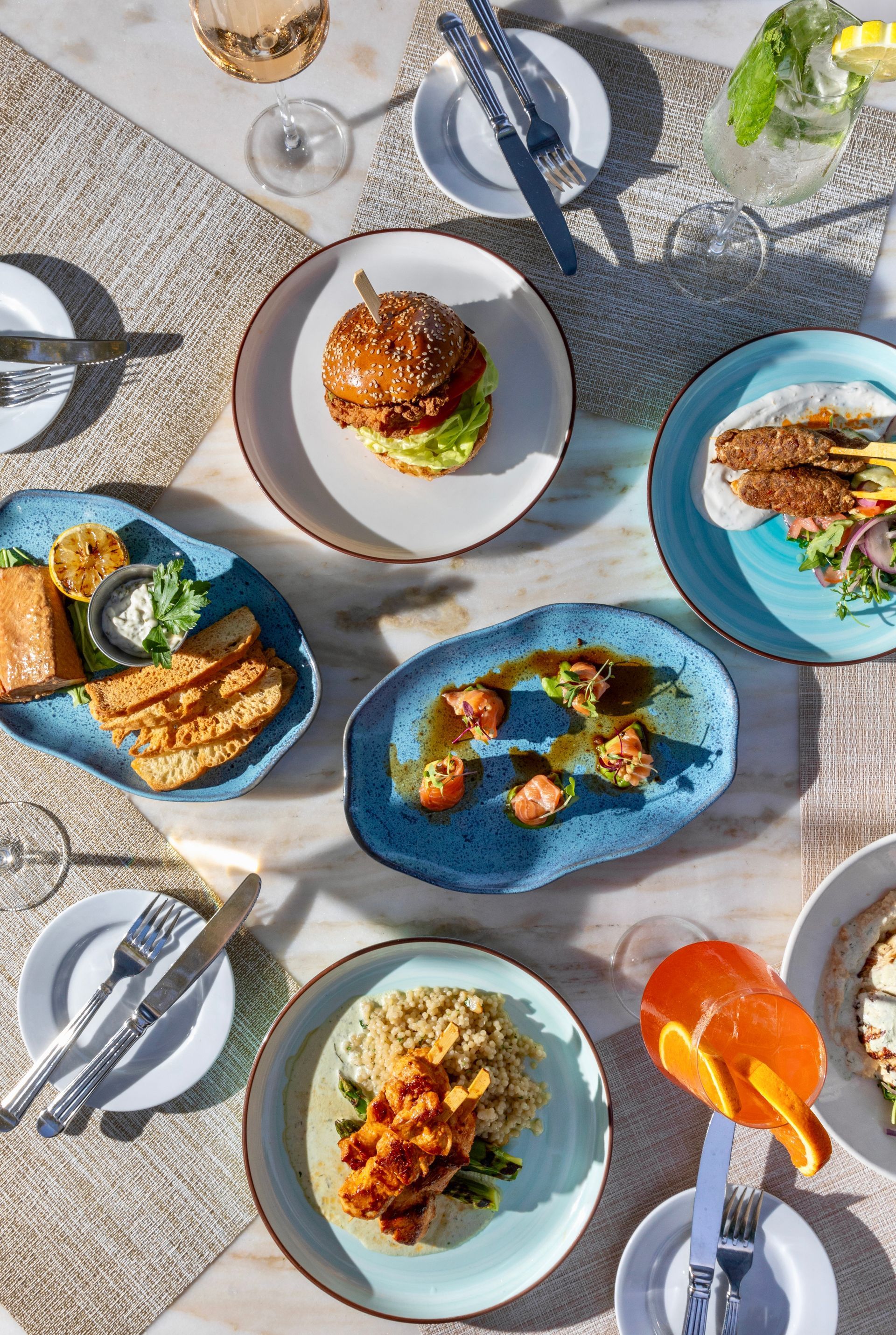 Assorted plated dishes on an outdoor table, with colorful food and drinks in bright sunlight.
