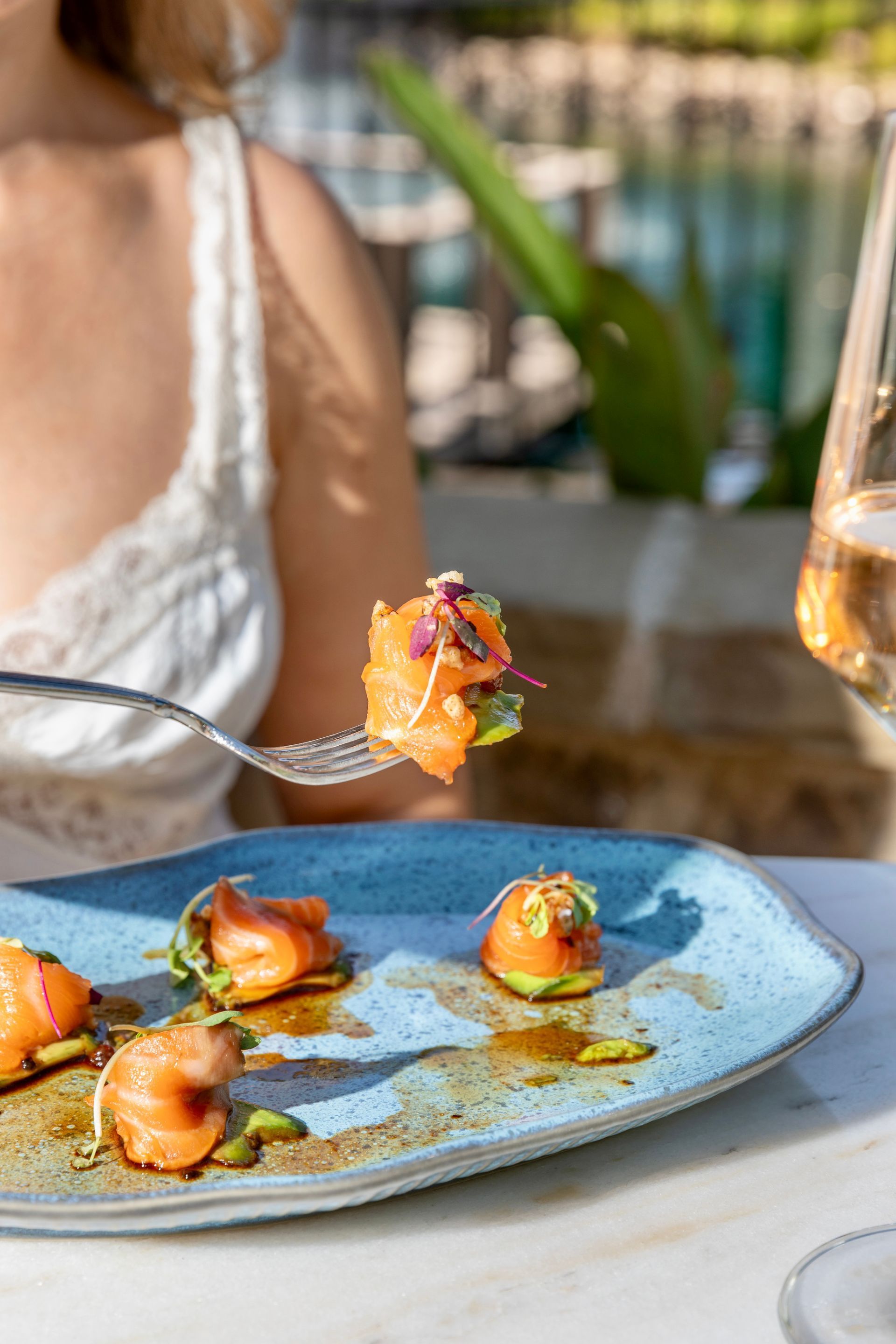 Blue plate with gourmet appetizers and a hand lifting a bite at an outdoor restaurant table