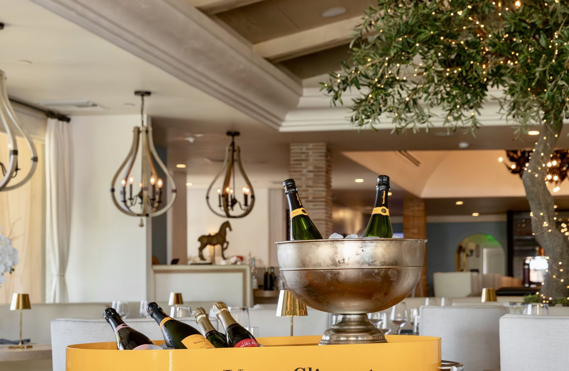 Restaurant interior with champagne bottles in ice bucket, decorative tree, and pendant lights.