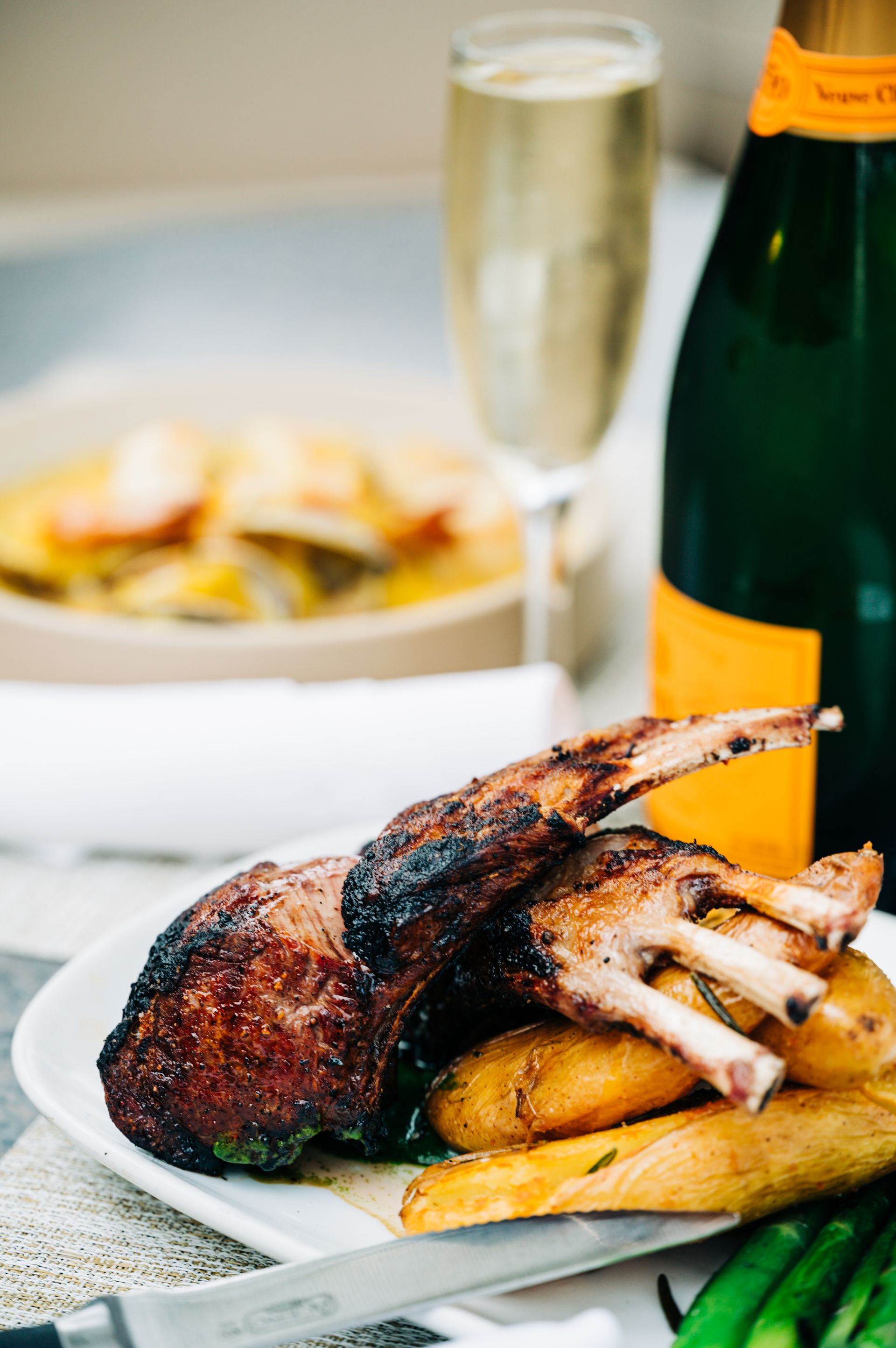 Grilled lamb chops with roasted potatoes, champagne, and side dish on a white plate.