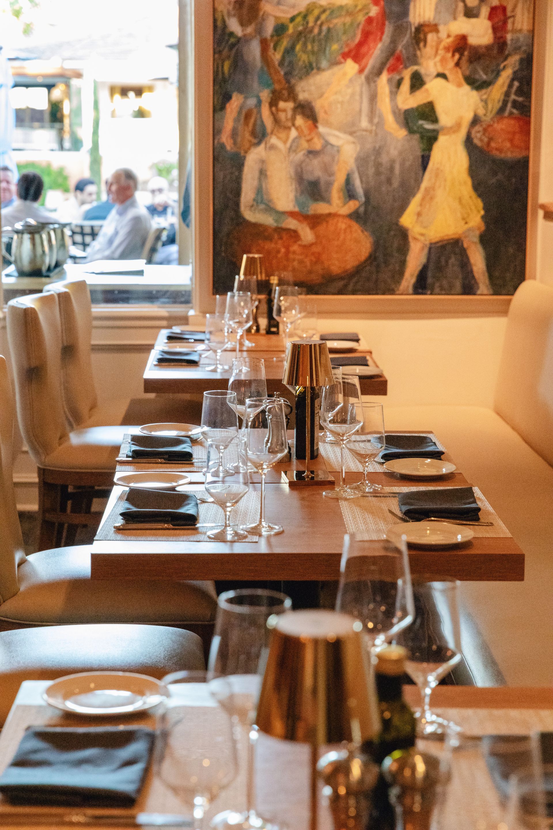 Restaurant table setting with glasses, plates, and art on the wall.