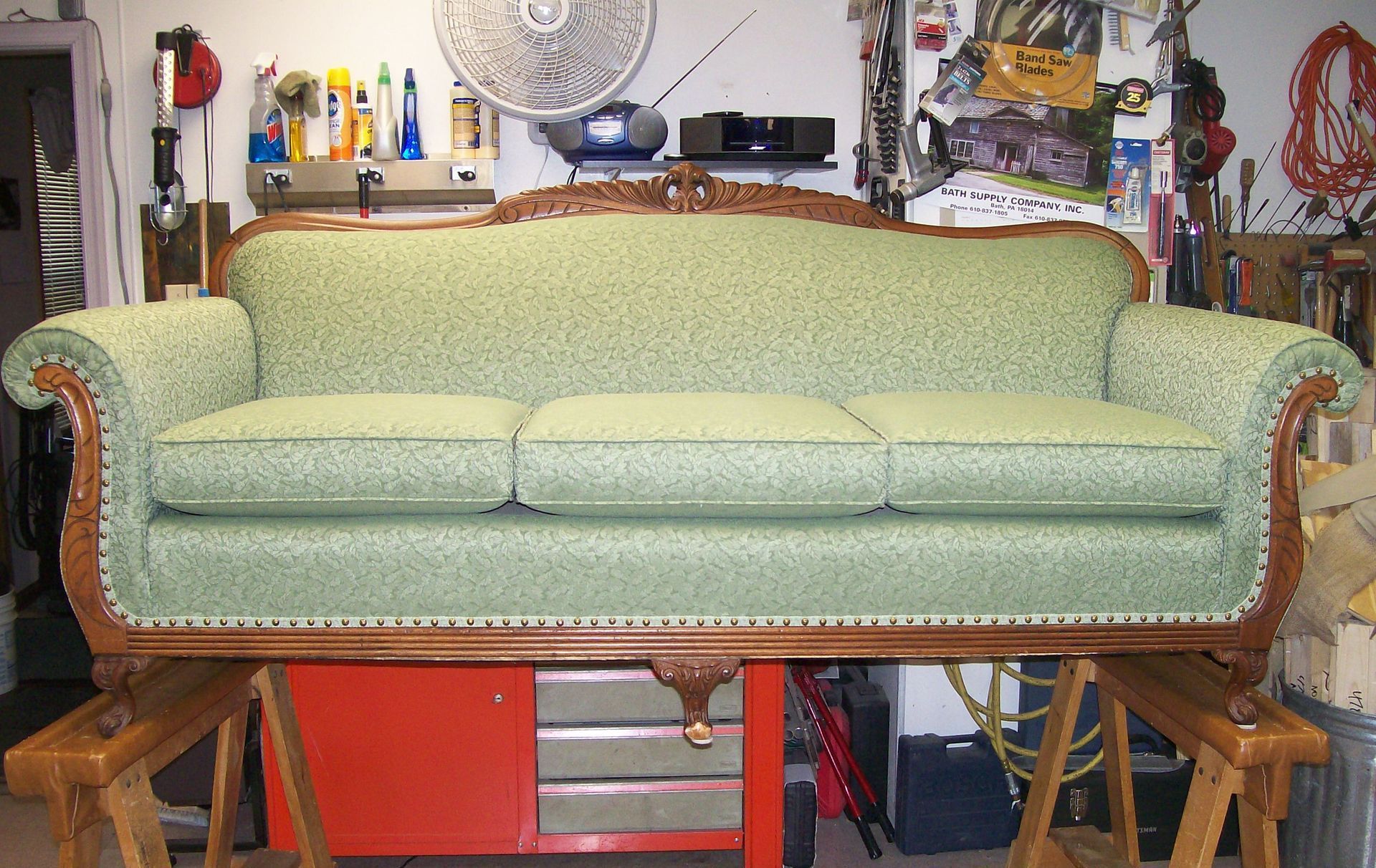 A green couch is sitting on a wooden table in a garage
