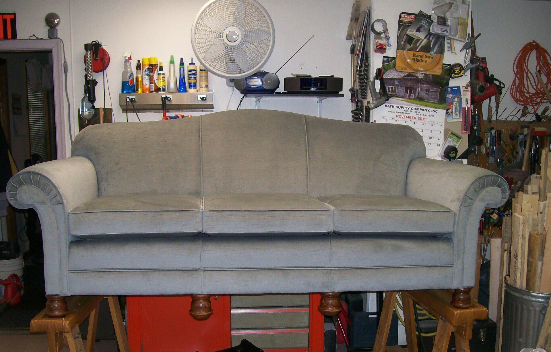 A grey couch is sitting on a wooden stand in a garage